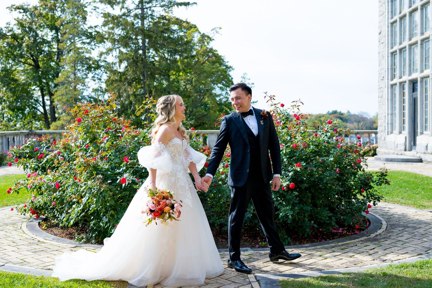 Wedding couple posing playfully outside stone building with rose garden.