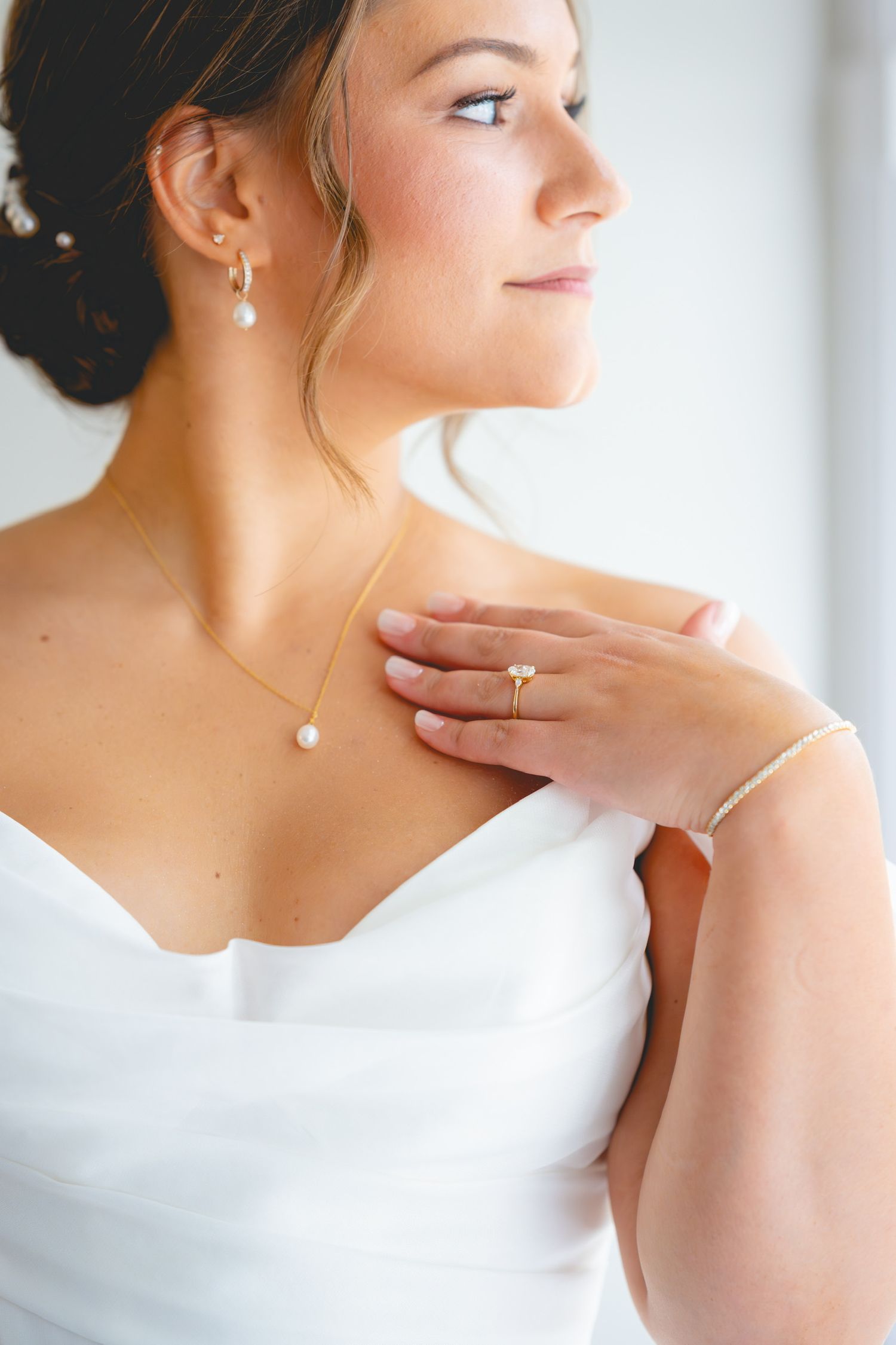 Elegant bridal portrait showing delicate jewelry and white dress details.