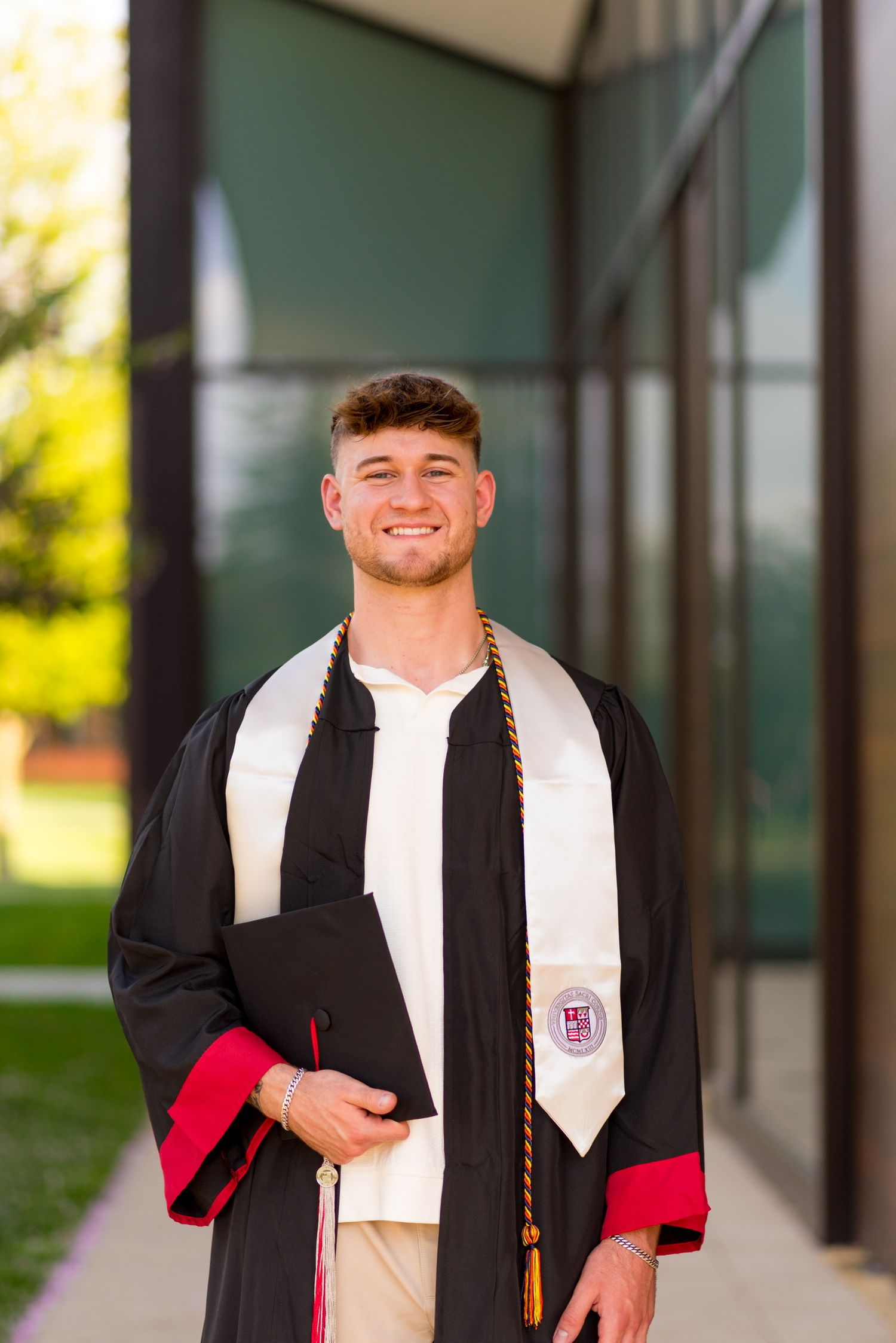 Sacred Heart University graduate in black cap and gown with red stole smiling for graduation photos.