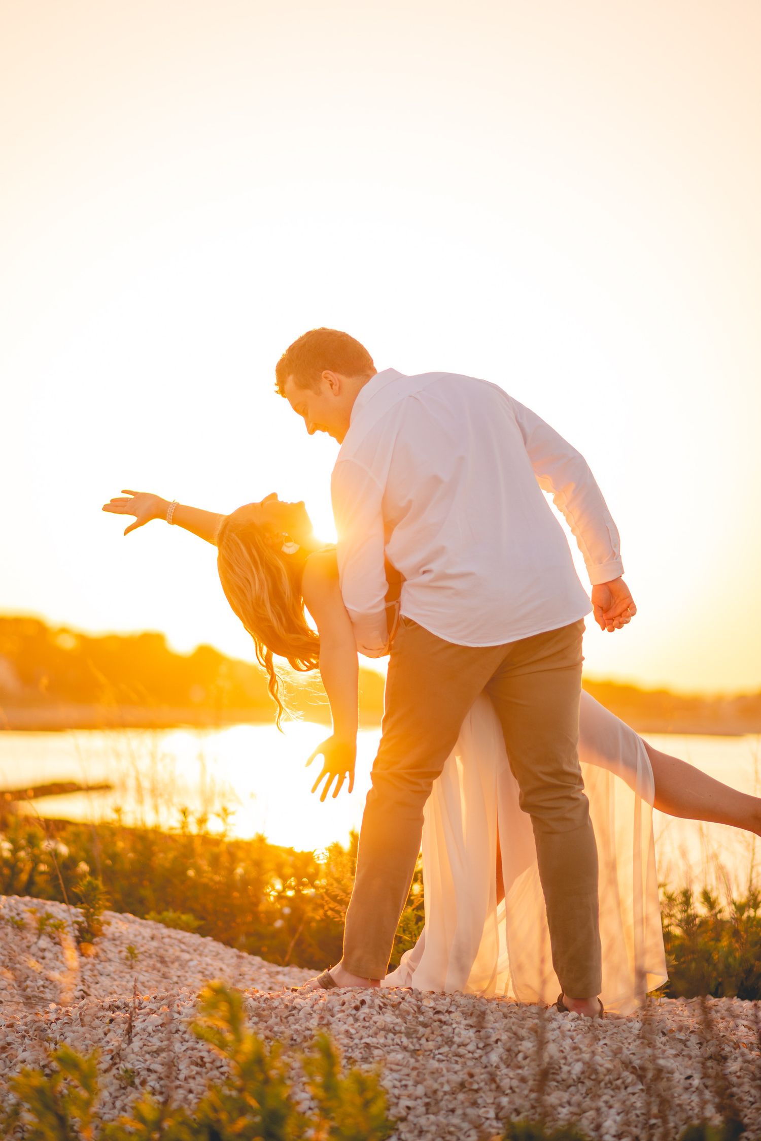 Silhouetted couple playfully posing against dramatic sunset over water.