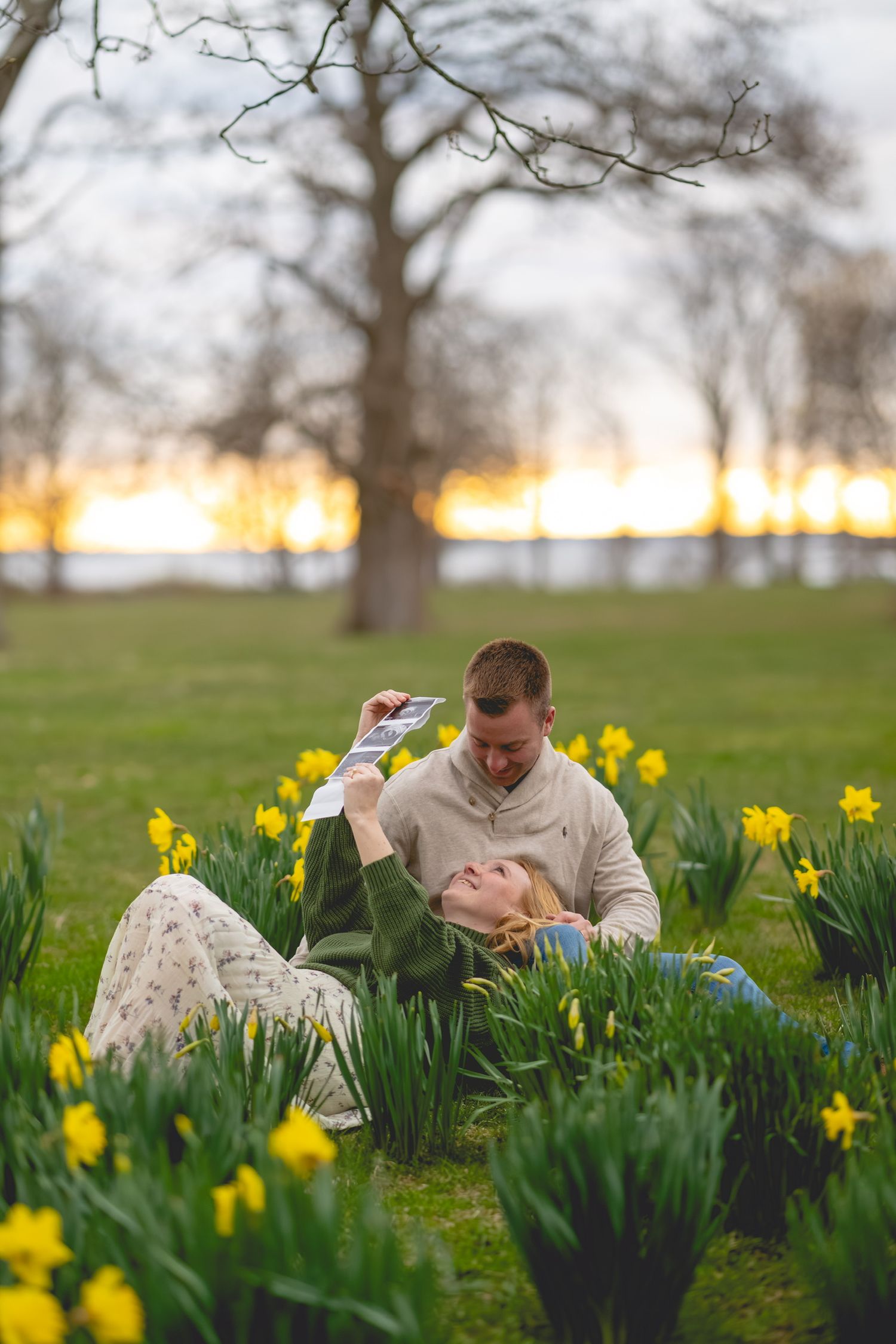 Couple lying in field of daffodils at sunset.