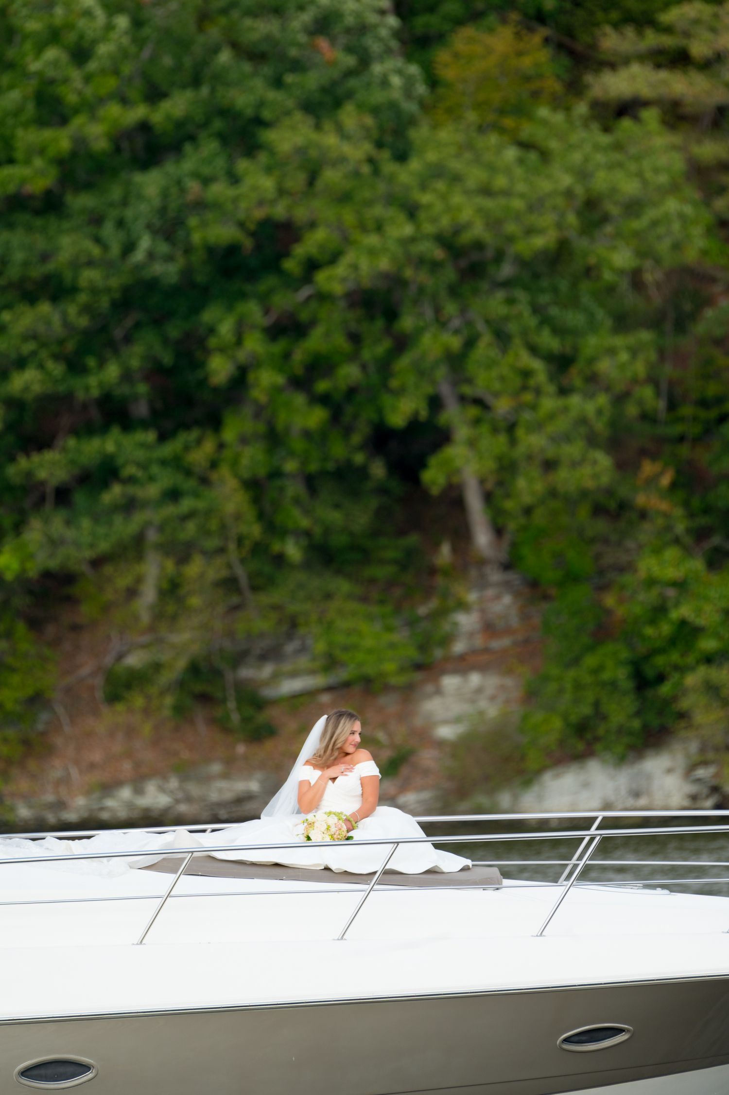 White yacht deck with railing against lush green forest background on a sunny day.
