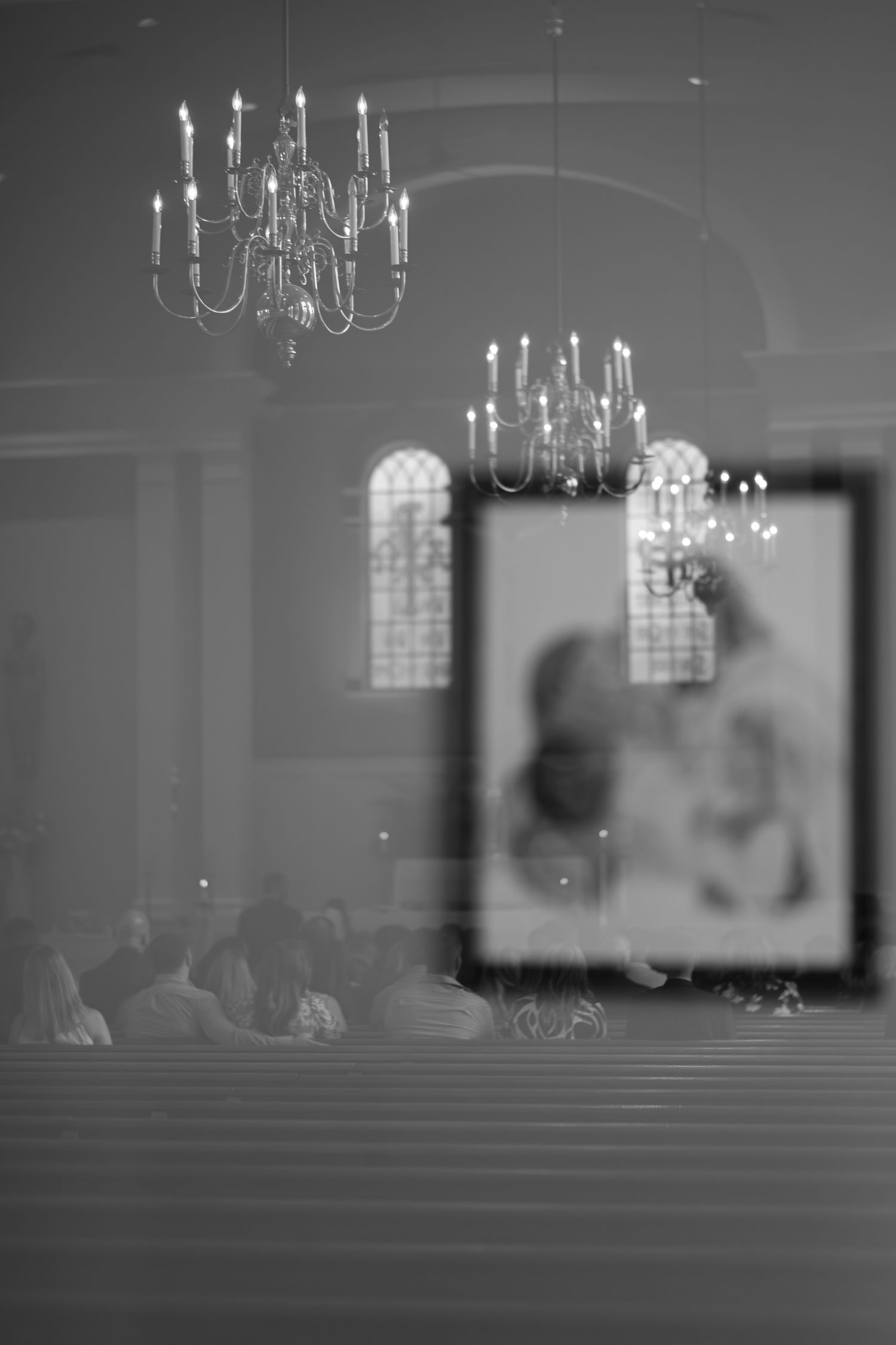 Black and white image of elegant chandeliers hanging in a reception hall with soft bokeh effect.