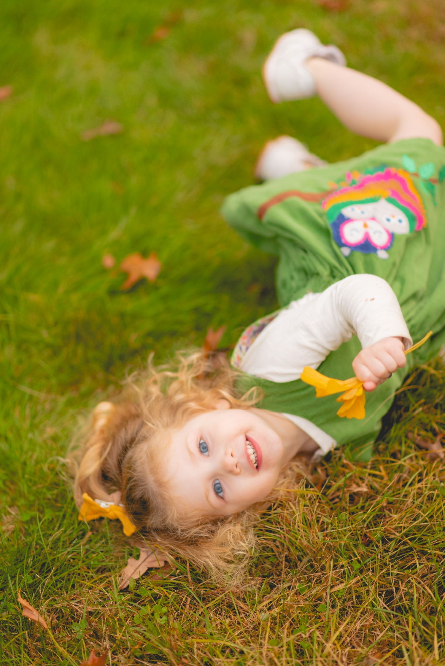 Child lying on grass surrounded by fallen autumn leaves.