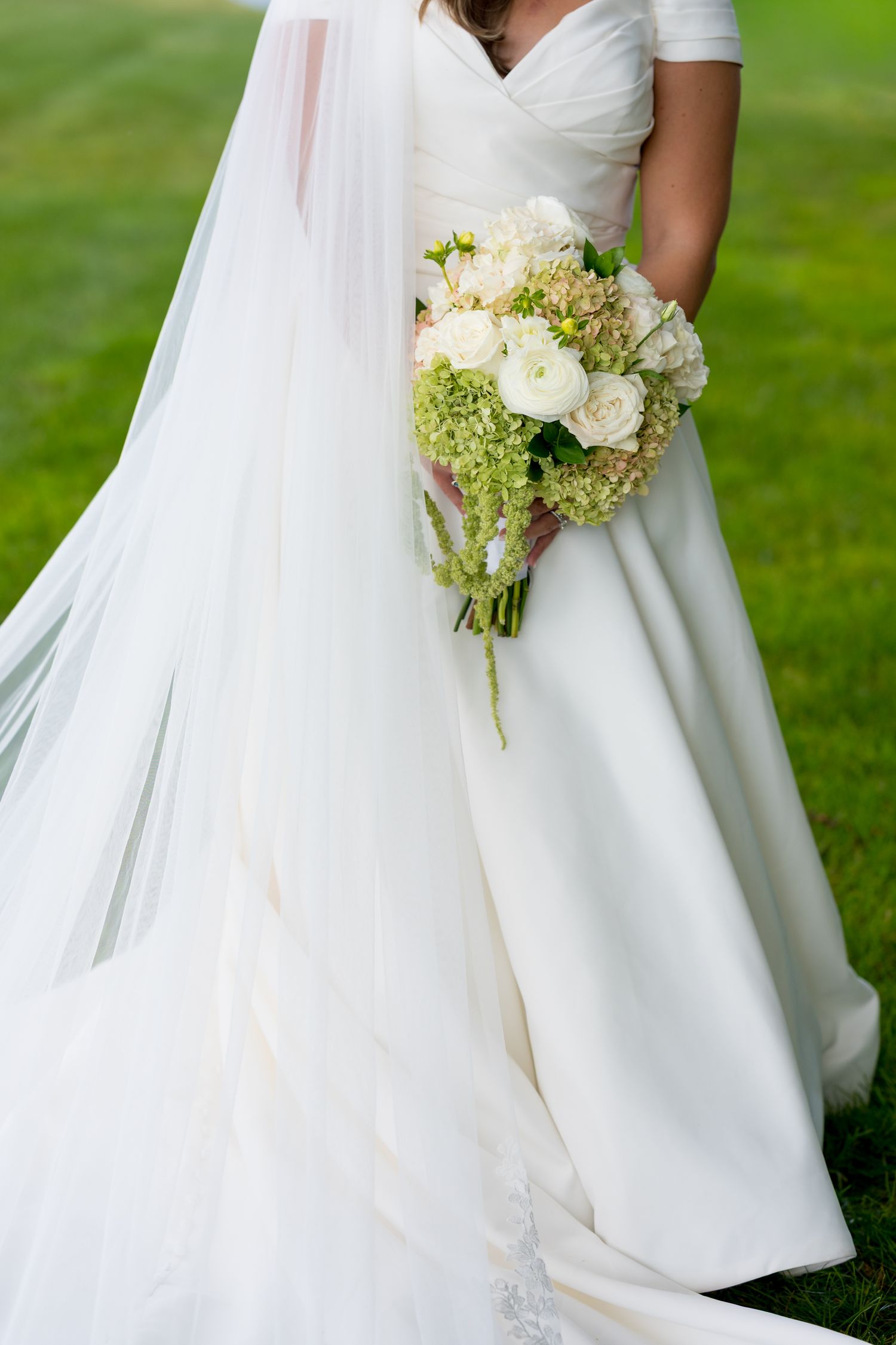 Elegant white wedding dress with flowing skirt and delicate bouquet of white roses and green hydrangeas.