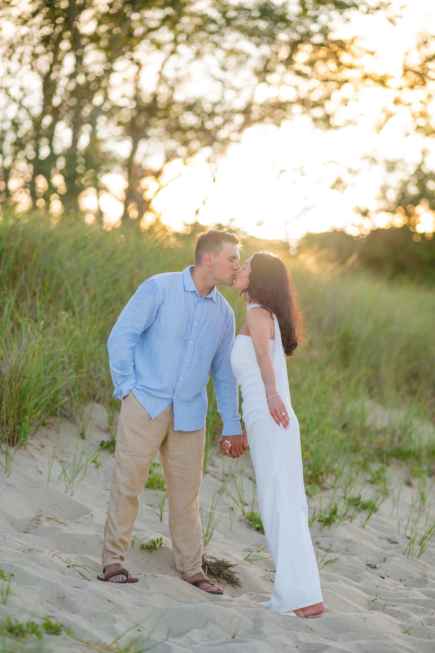 Romantic couple shares tender moments on sandy beach dunes at sunset in summer.