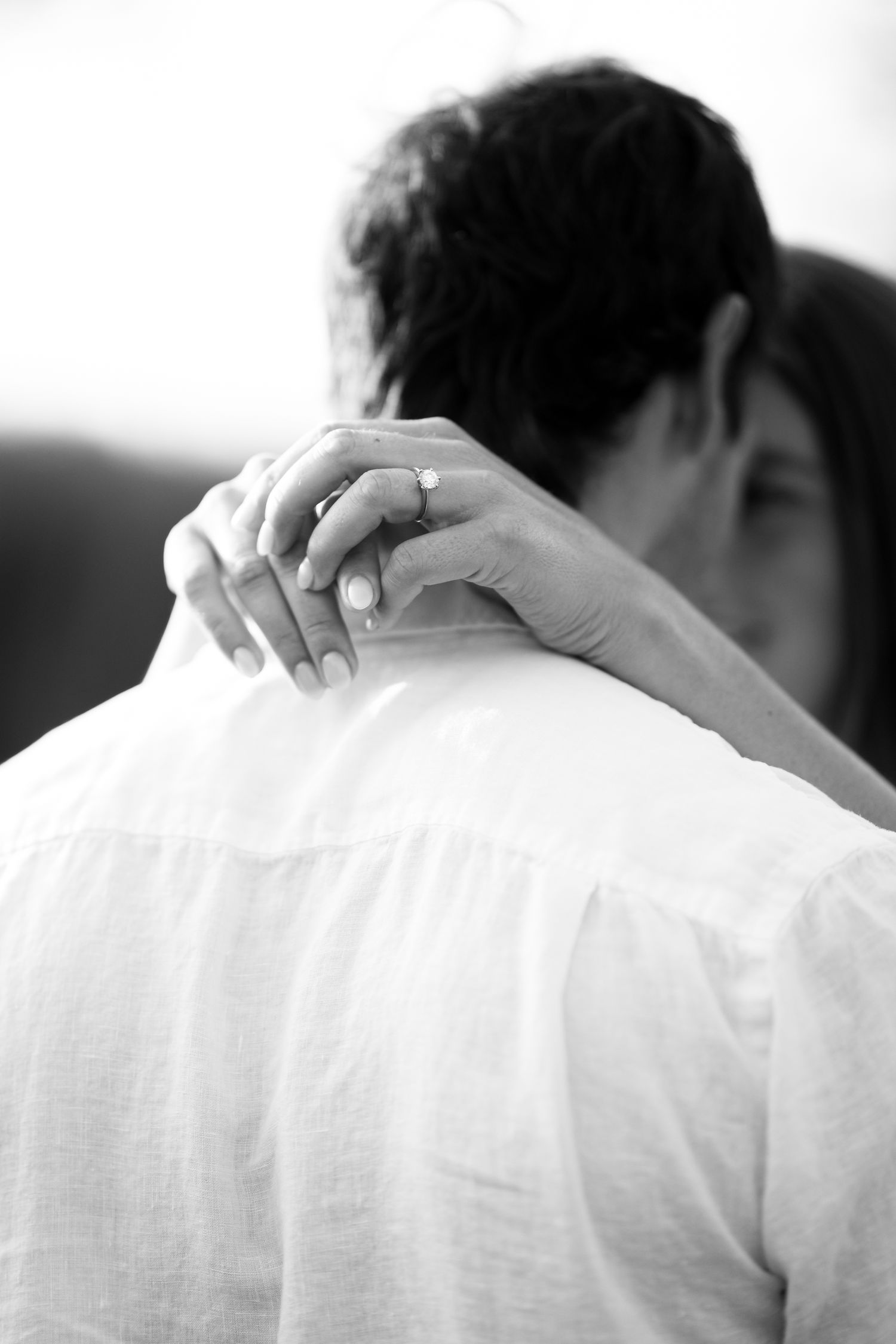 Black and white photo of hands resting on shoulders in an intimate embrace wearing white linen clothing.