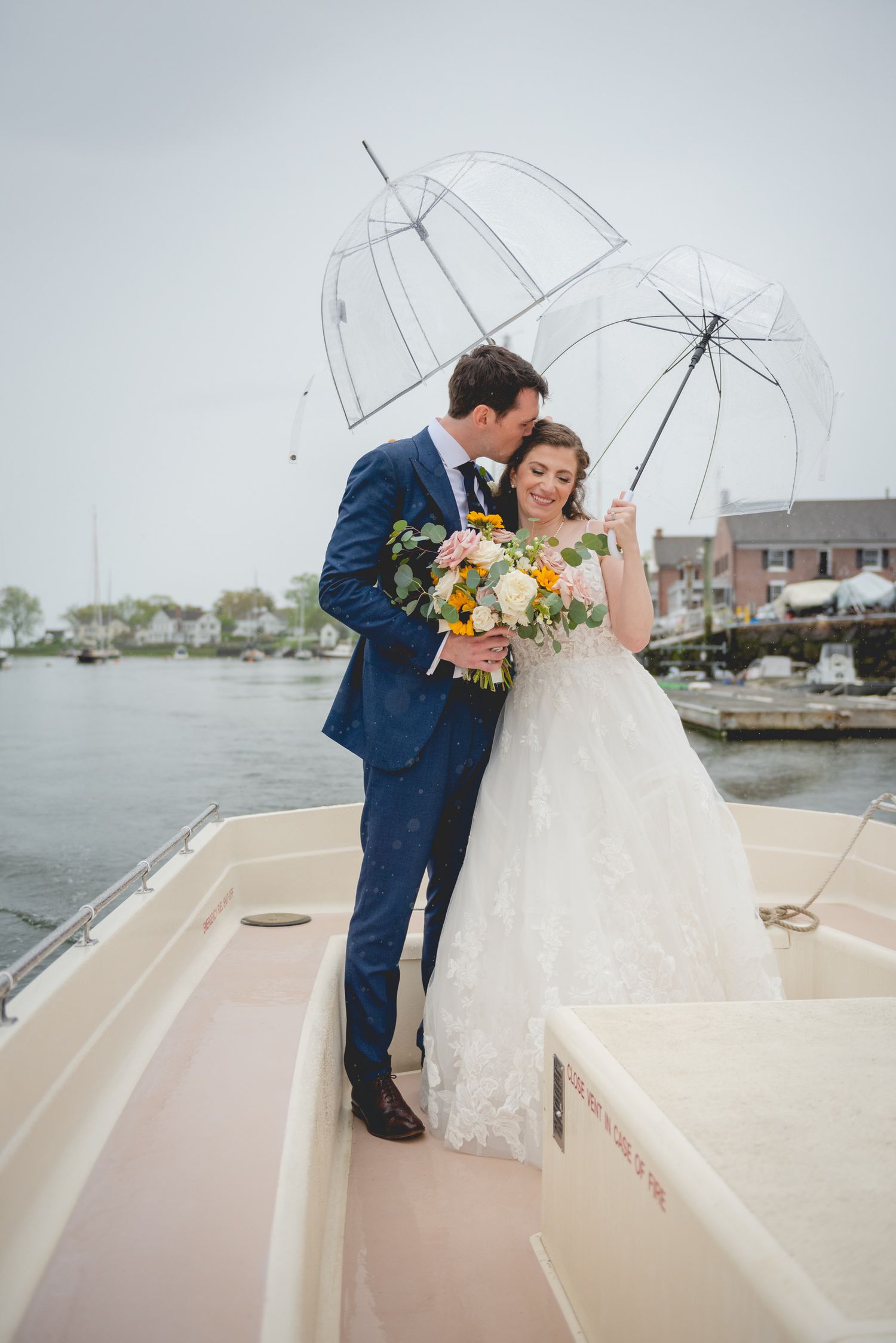 Couple with clear umbrellas sharing romantic moment on dock during rainy wedding day.
