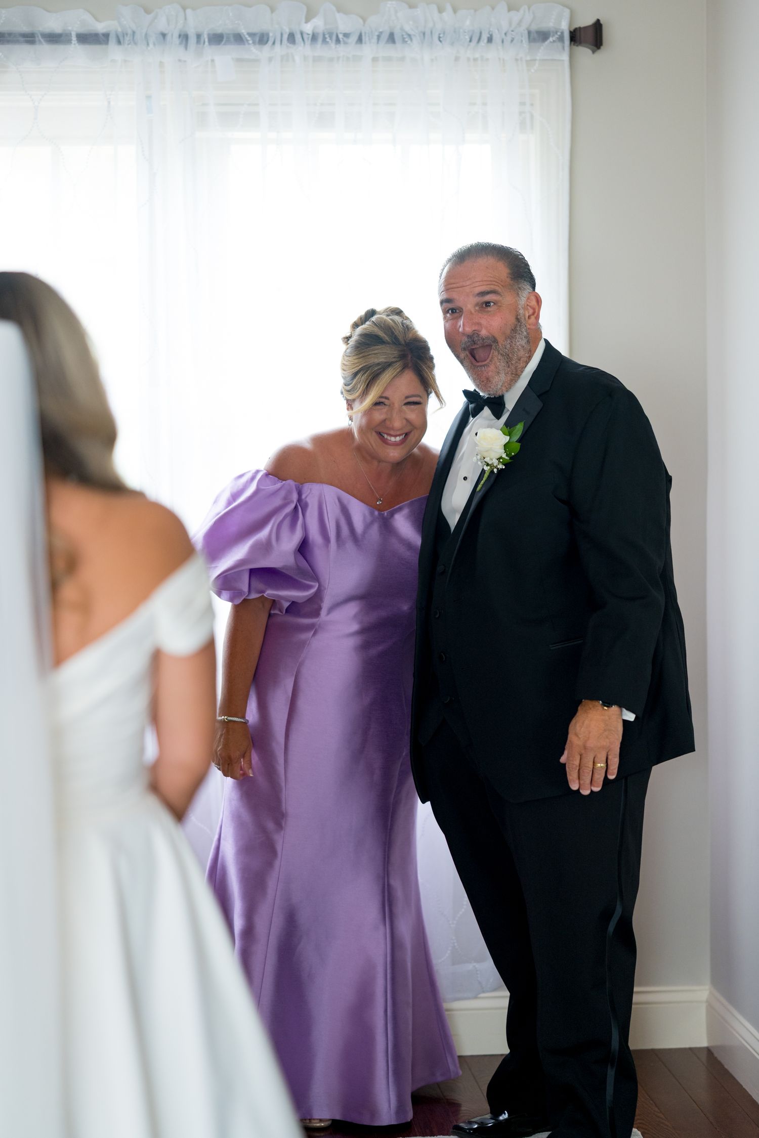 Wedding party members in formal attire including purple dresses and black tuxedos pose together.