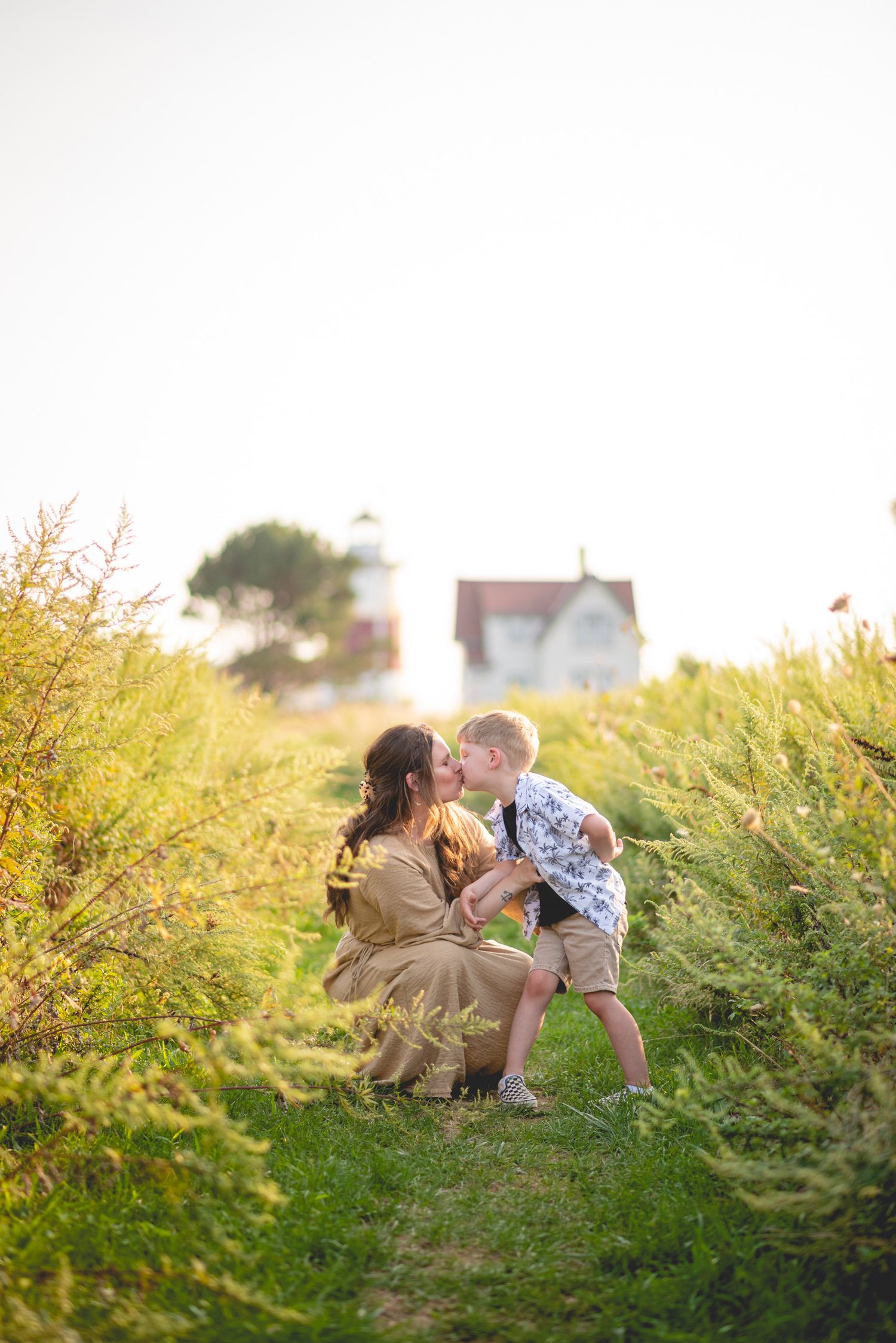 Family sharing intimate moments in tall grass during sunset with a house in the background.