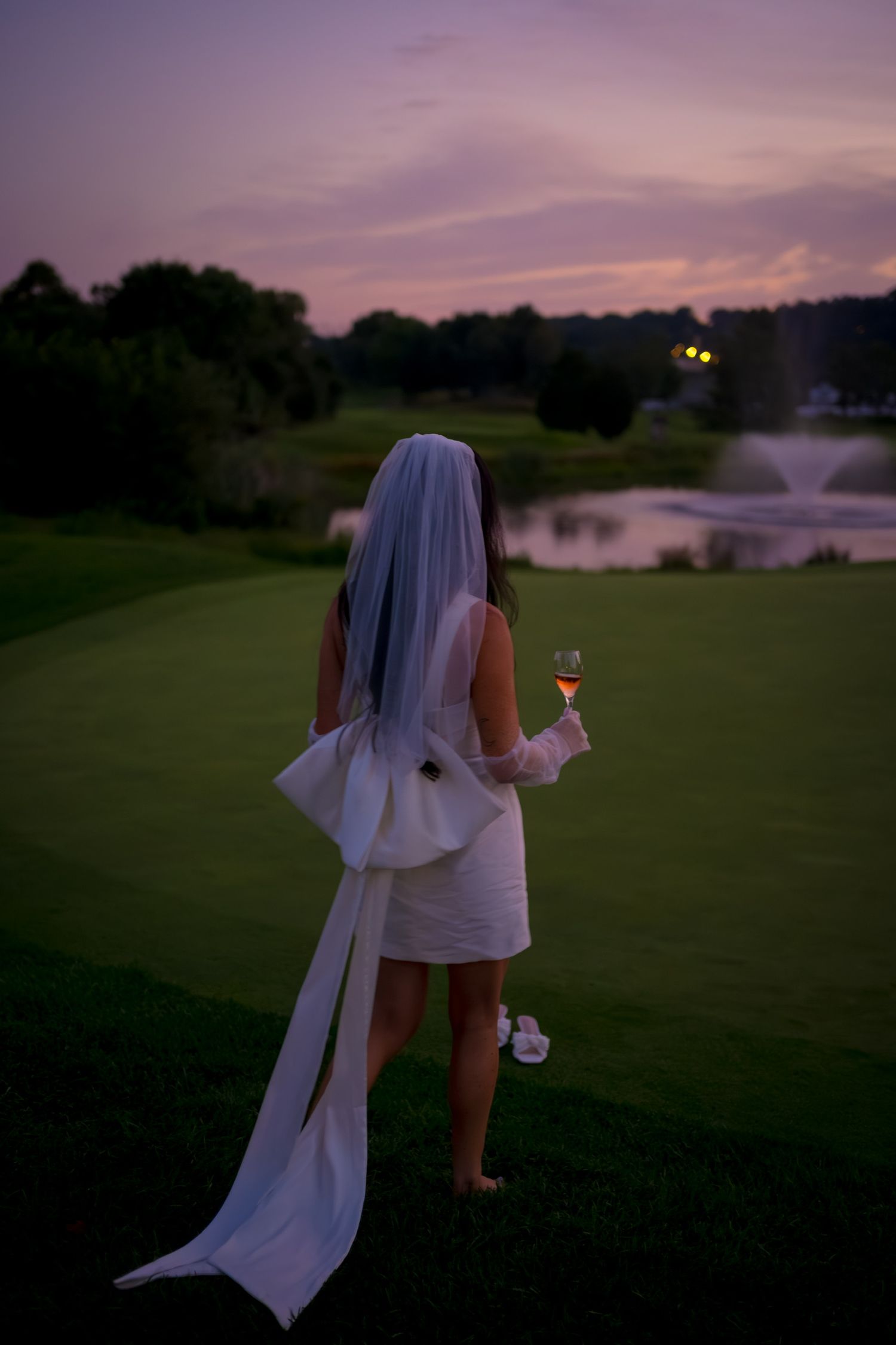 White flowing dress and veil silhouetted against sunset sky on golf course.