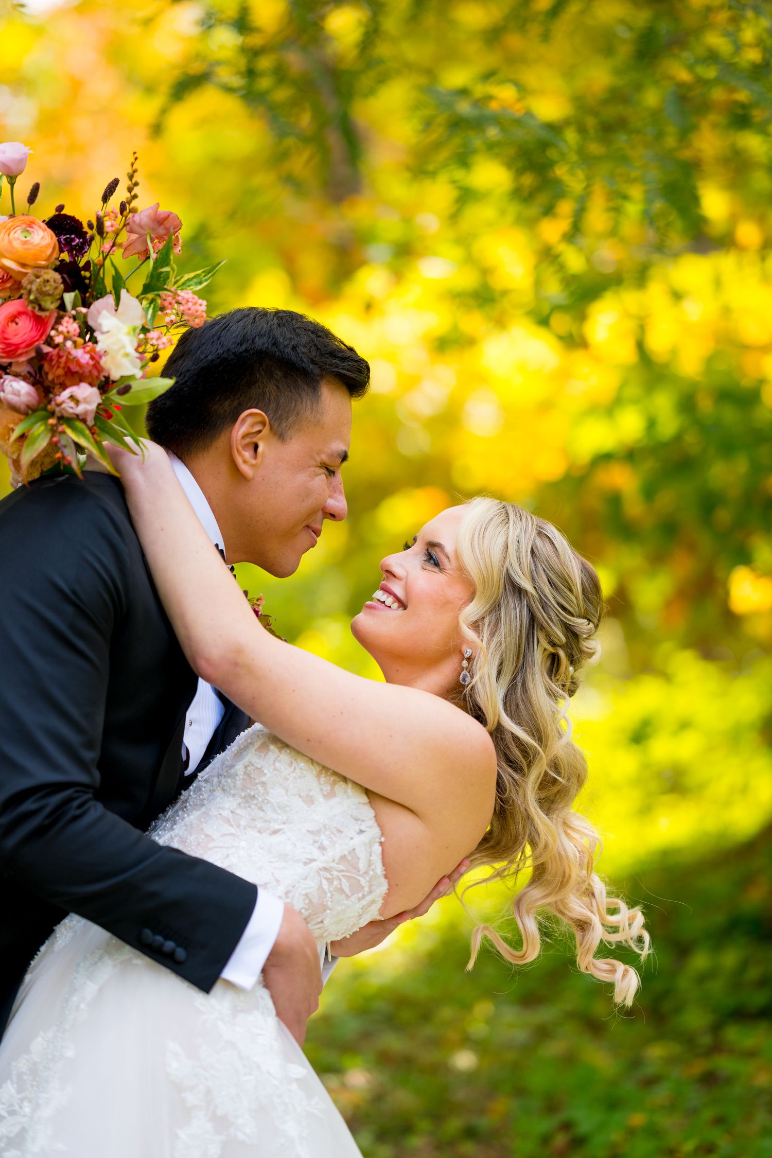 Joyful wedding couple dancing outdoors against vibrant autumn foliage.