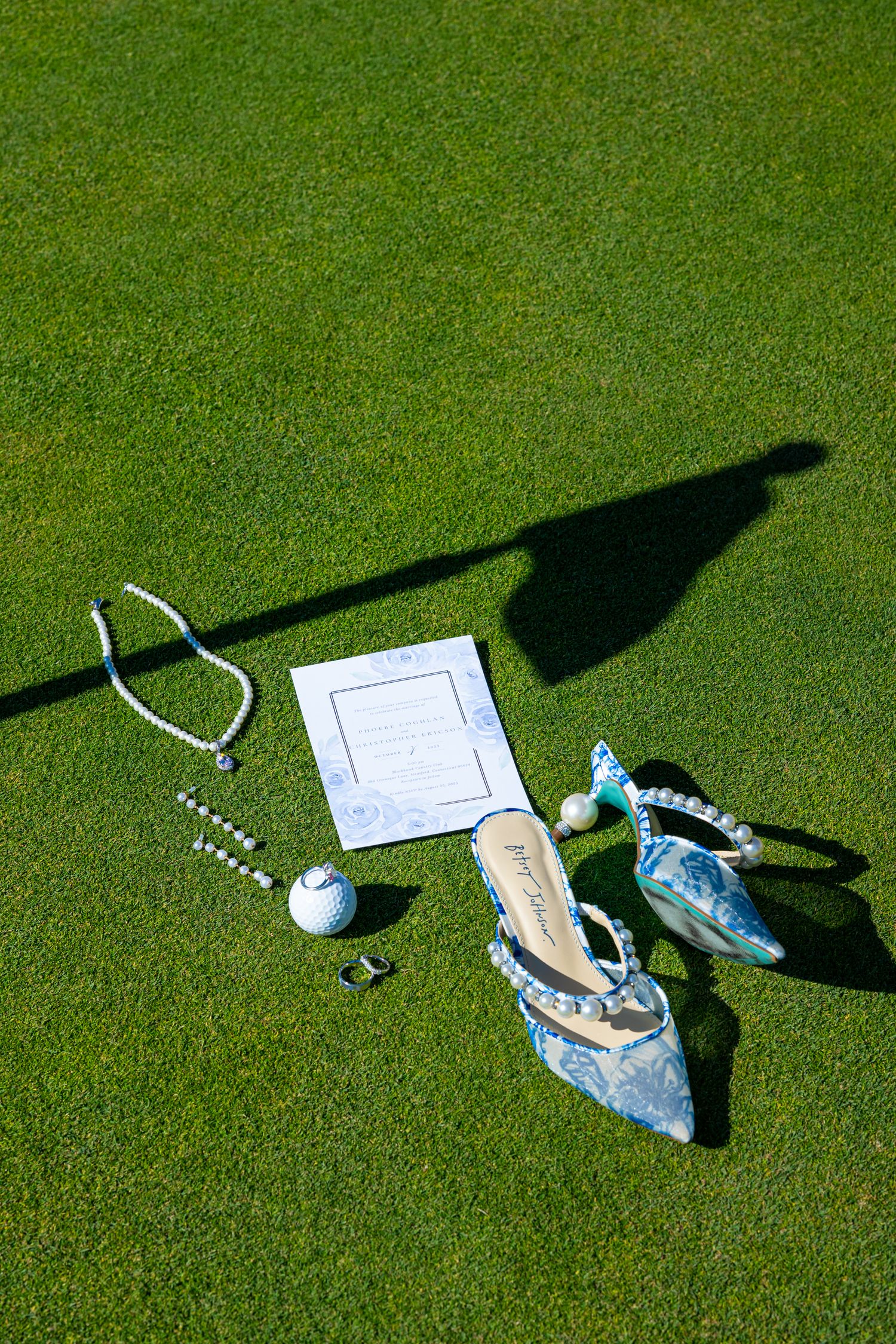 Wedding accessories and shoes cast shadows on bright green grass.