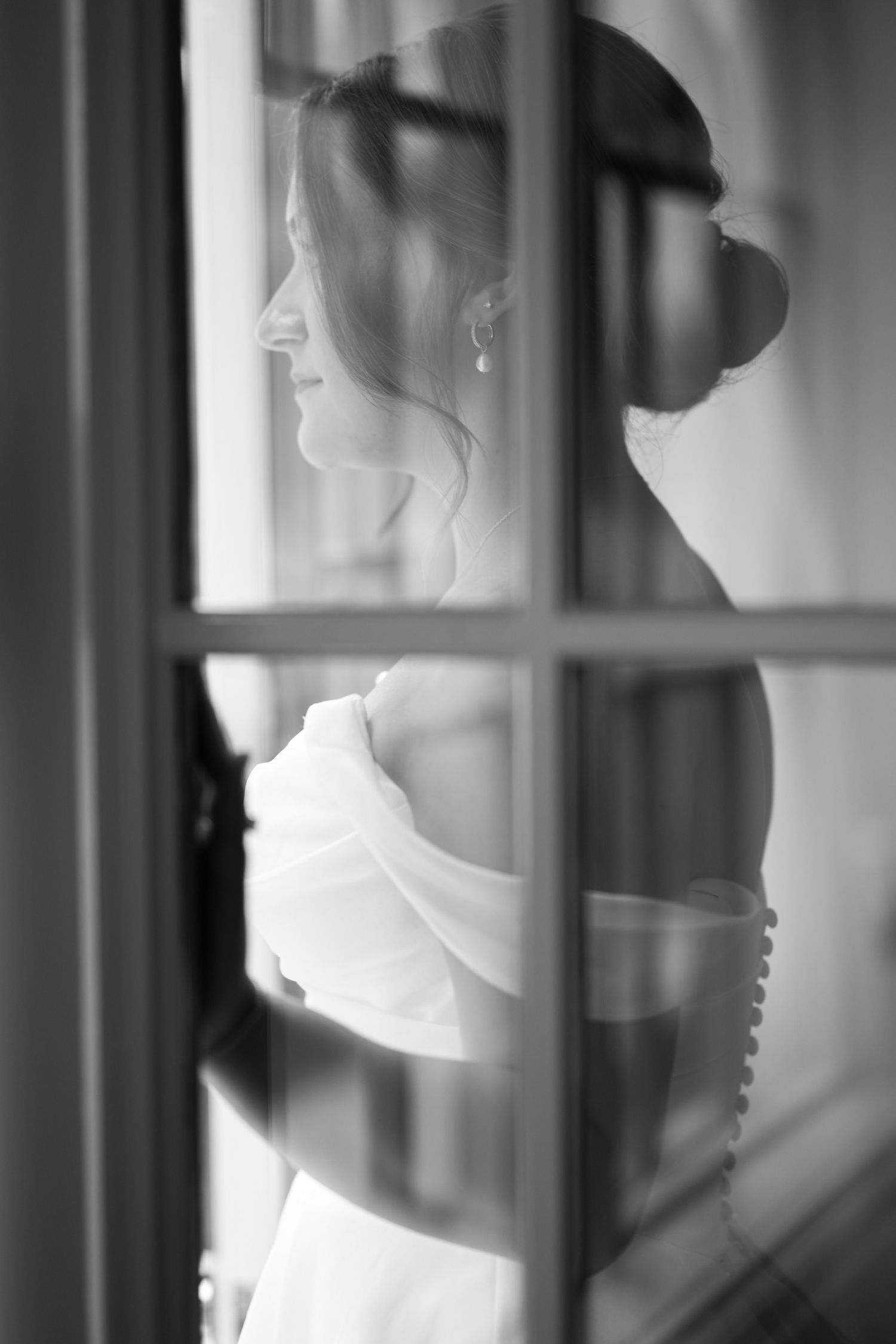 Artistic black and white silhouette of bride through window panes creating dramatic shadows.