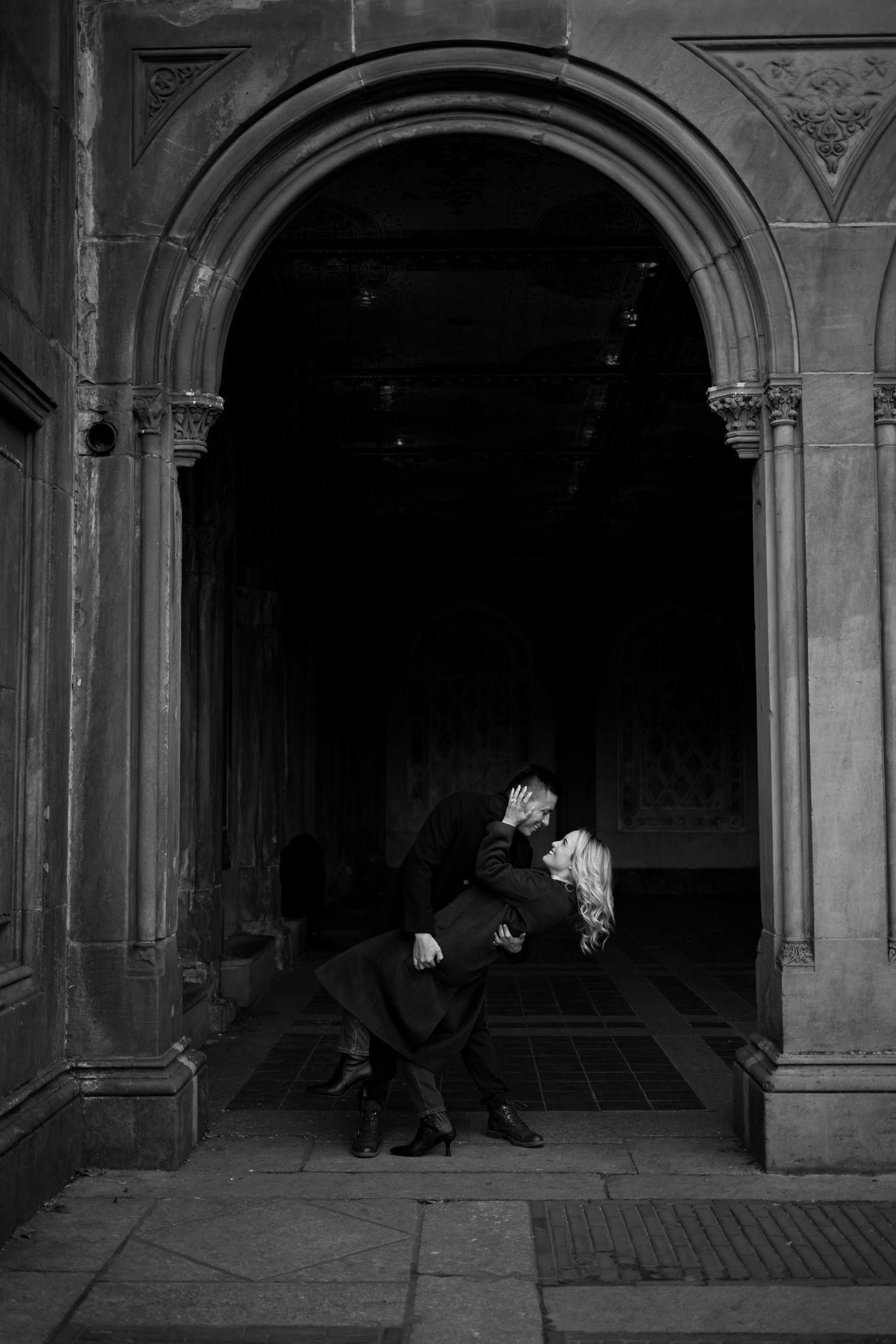Romantic couple sharing an intimate moment under a grand stone archway in Central Park in Manhattan, New York.
