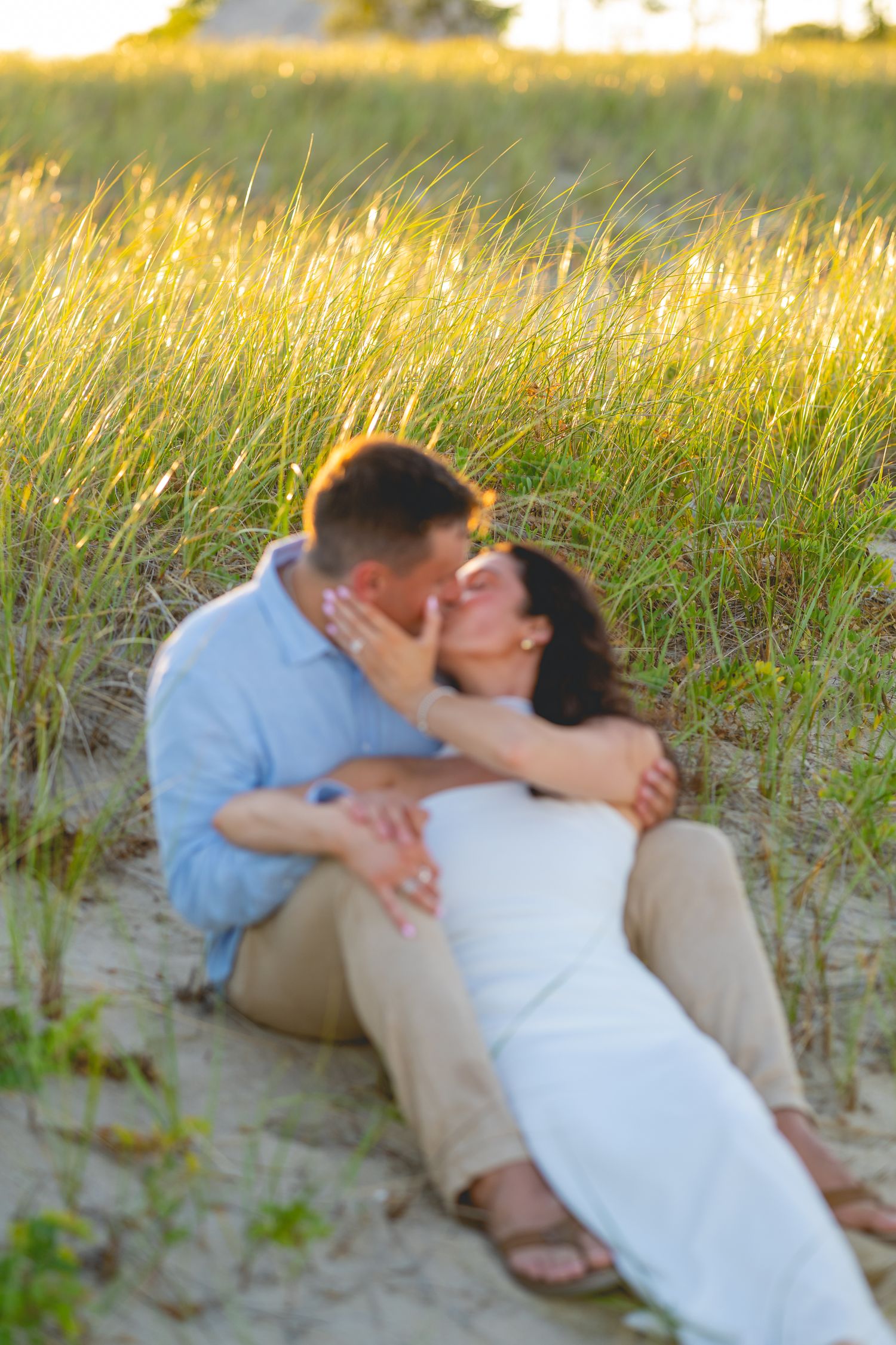 Couple reclines together on sandy beach during golden hour photography session at Chatham Lighthouse Beach in Chatham, Massachusetts.