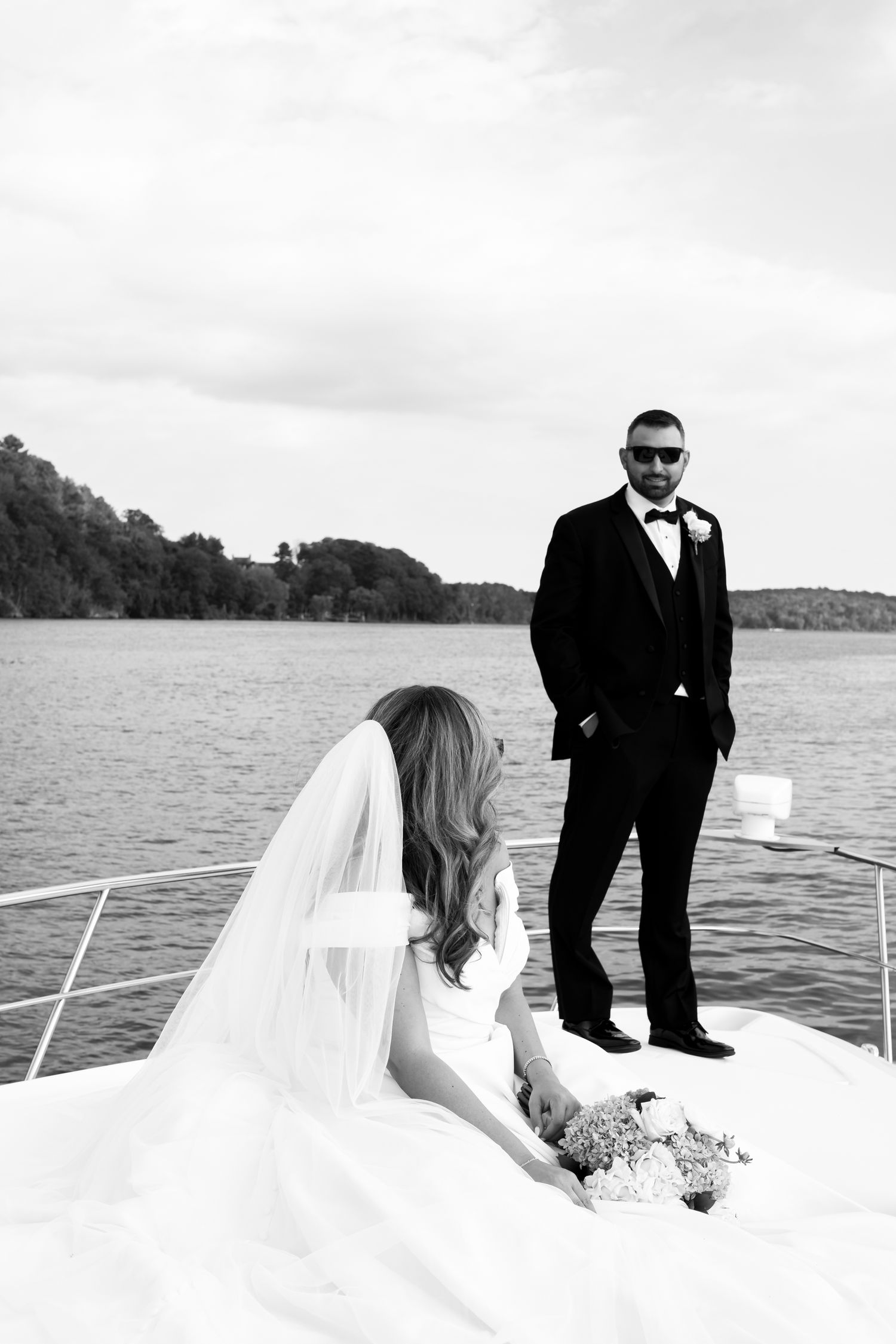 Wedding couple poses on boat deck with lake and shoreline in background.