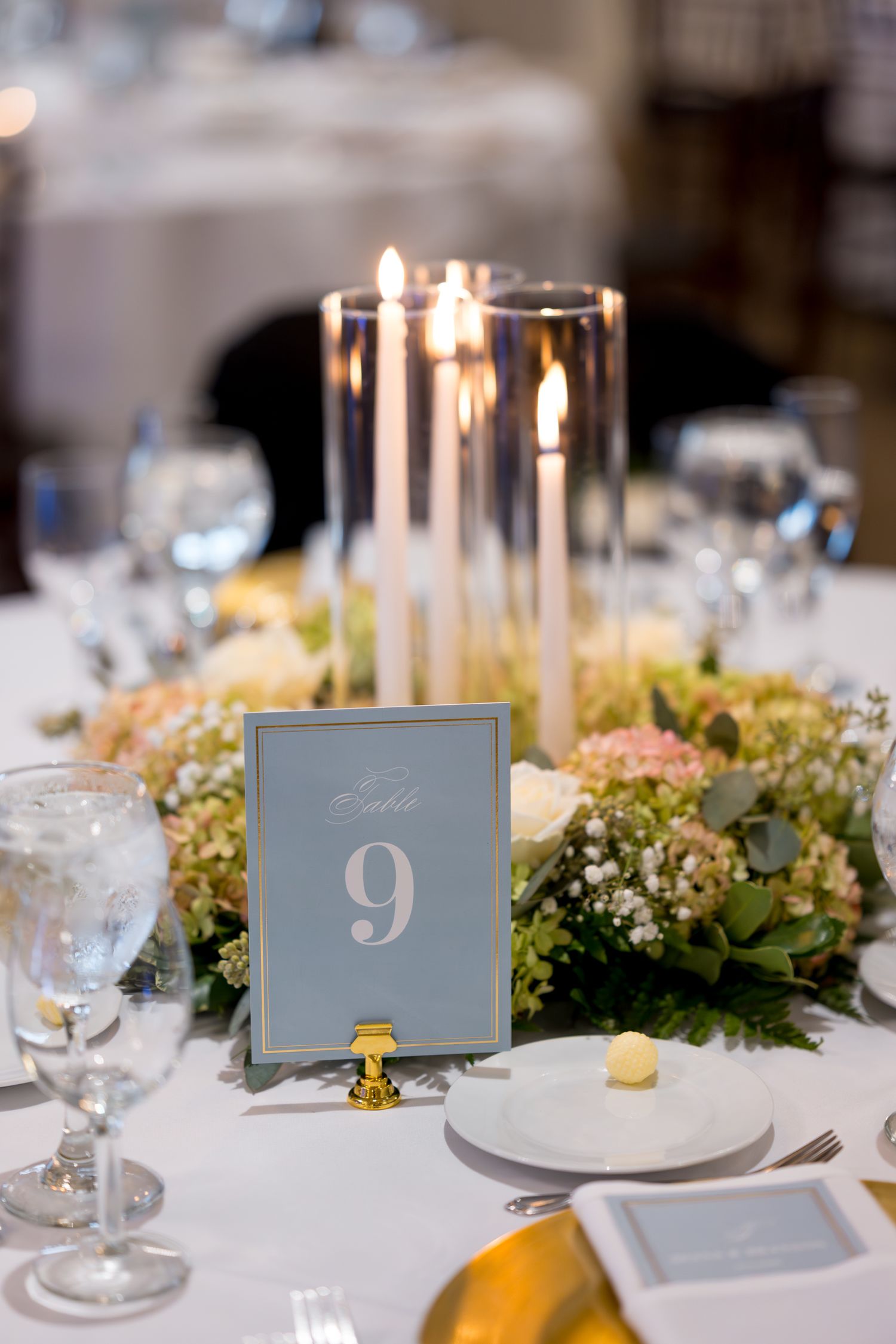 Elegant wedding reception table settings with blue table numbers, candles and floral centerpieces.