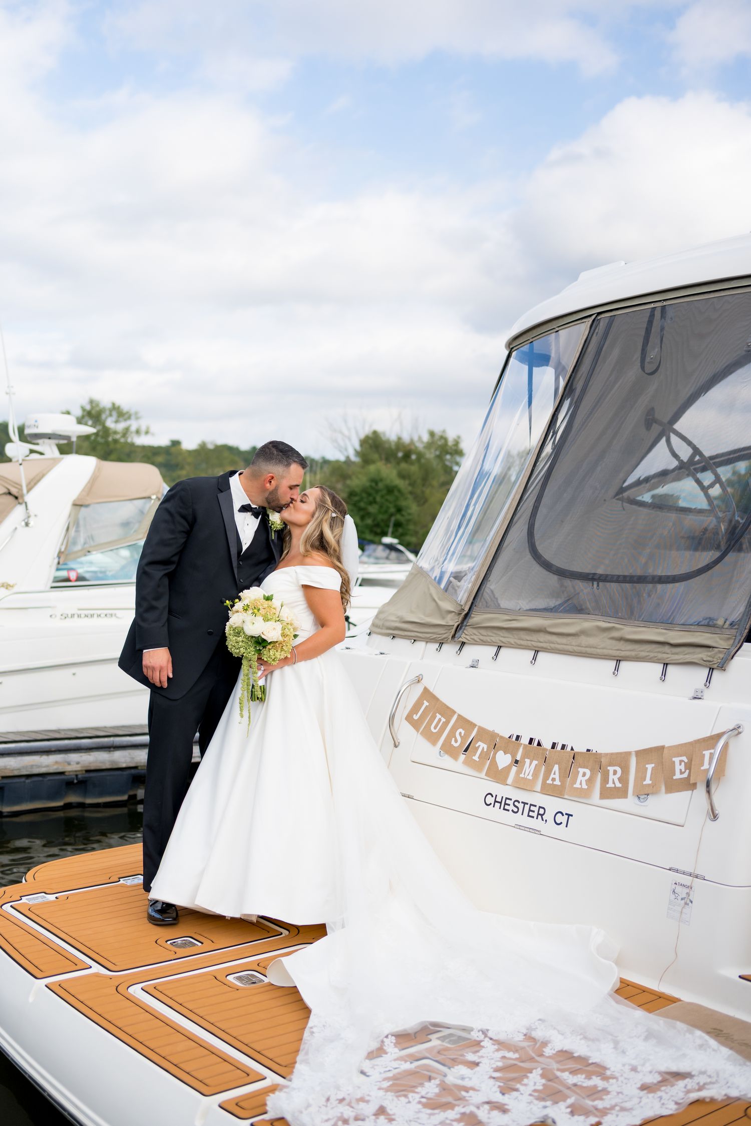 Newlyweds share romantic moment on yacht deck with white dress flowing in breeze.