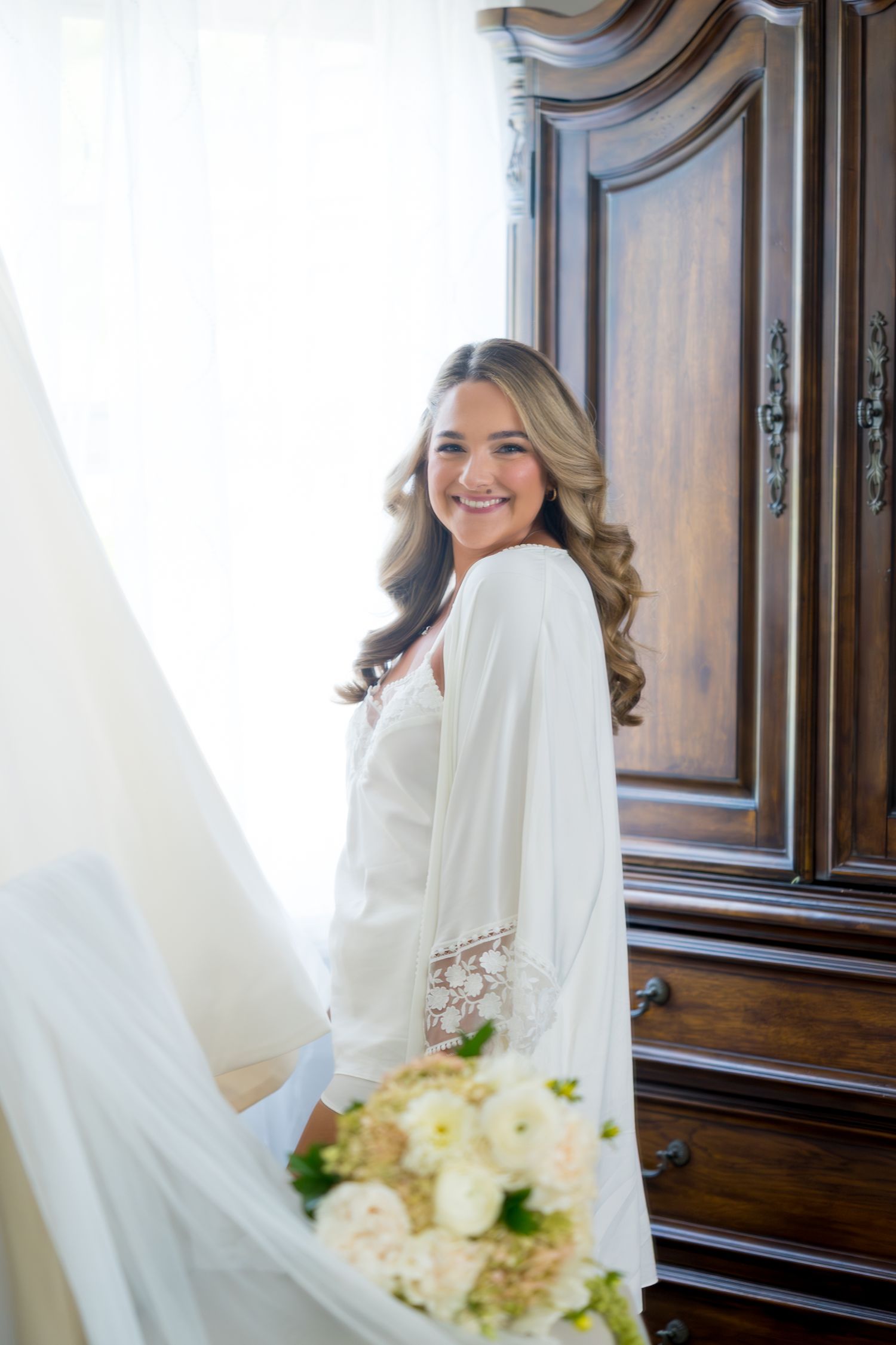 Elegant bridal portrait in white veil and gown against dark wooden doors with soft lighting.