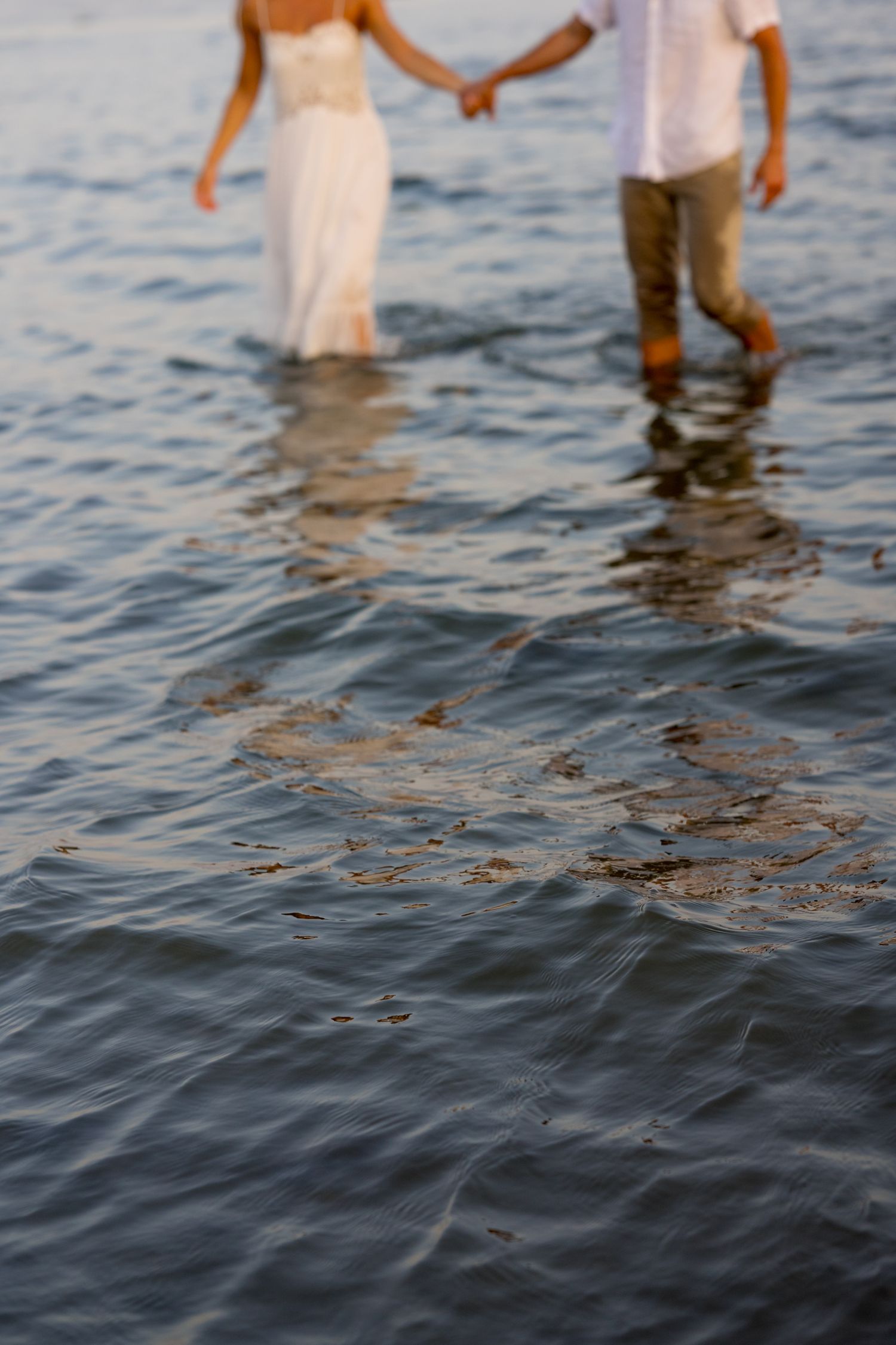 Legs of a couple standing in shallow ocean water during sunset.