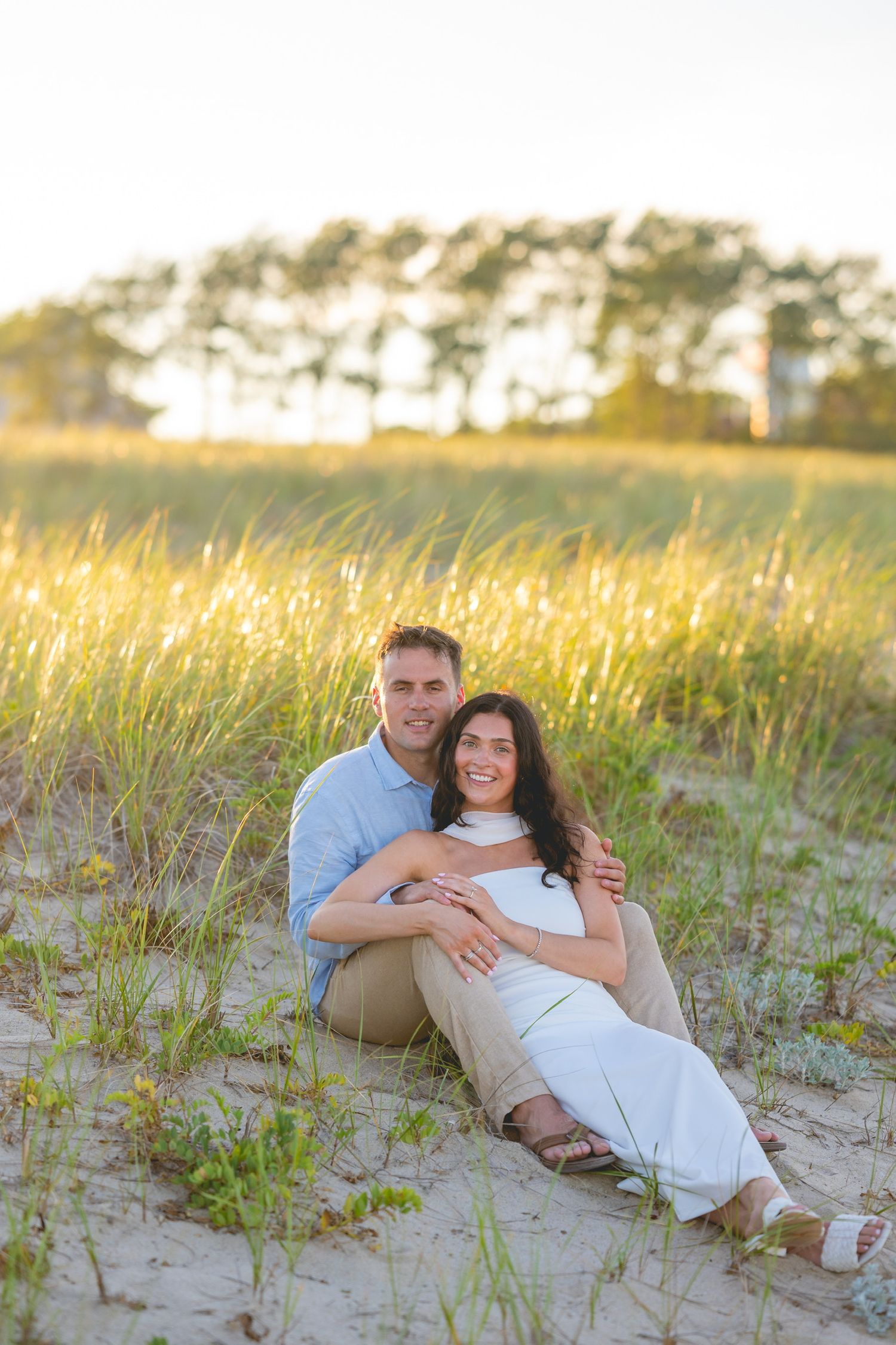 A couple relaxes together on sandy beach dunes during golden hour in Chatham, Massachusetts.