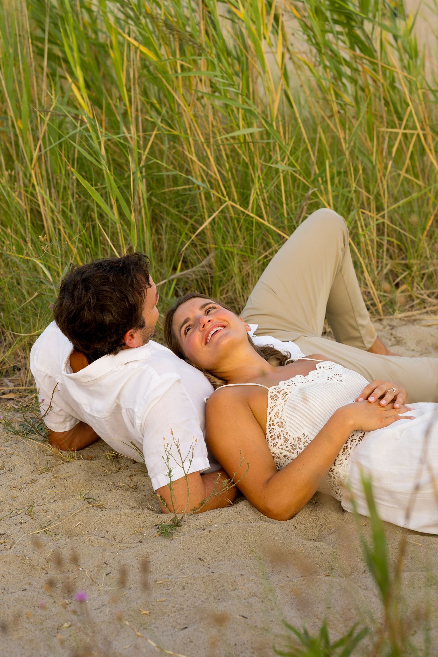 Couple lying together on beach sand surrounded by tall grass at sunset in Westport, Connecticut.