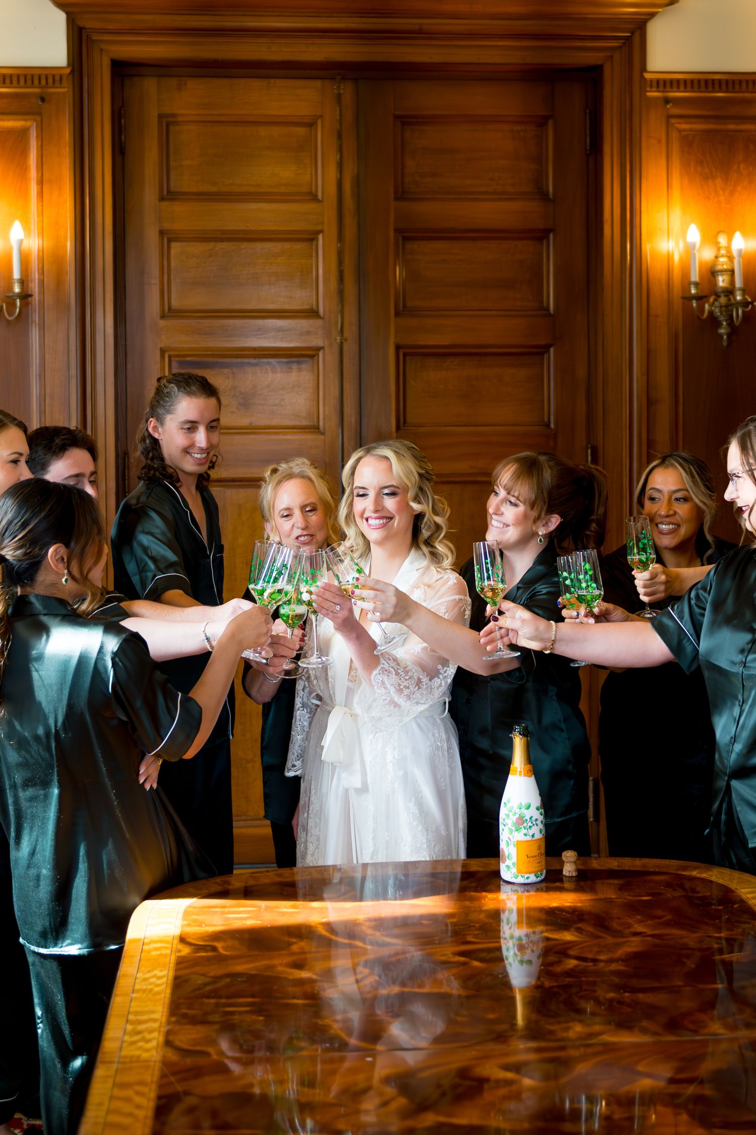 Wedding party raises champagne glasses for a celebratory toast in an elegant wood-paneled room with candlelight.