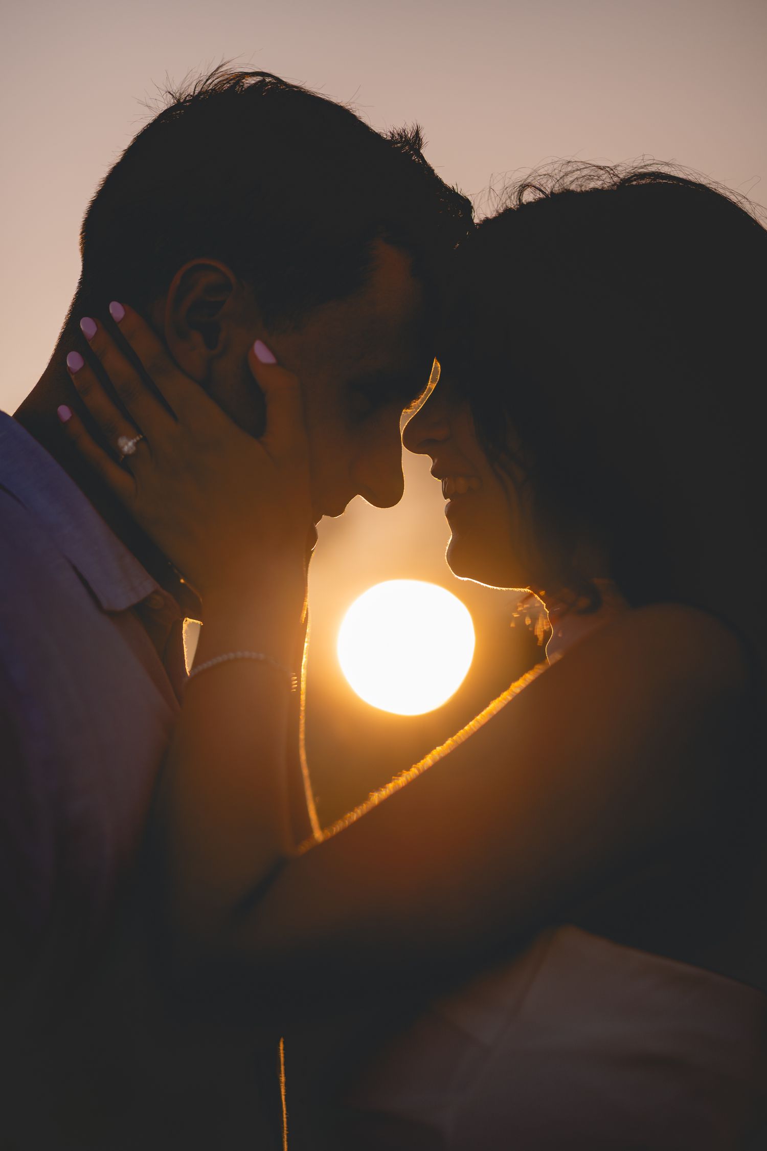 A silhouetted couple in profile sharing a romantic moment against a dramatic sunset creating a glowing backlit effect.