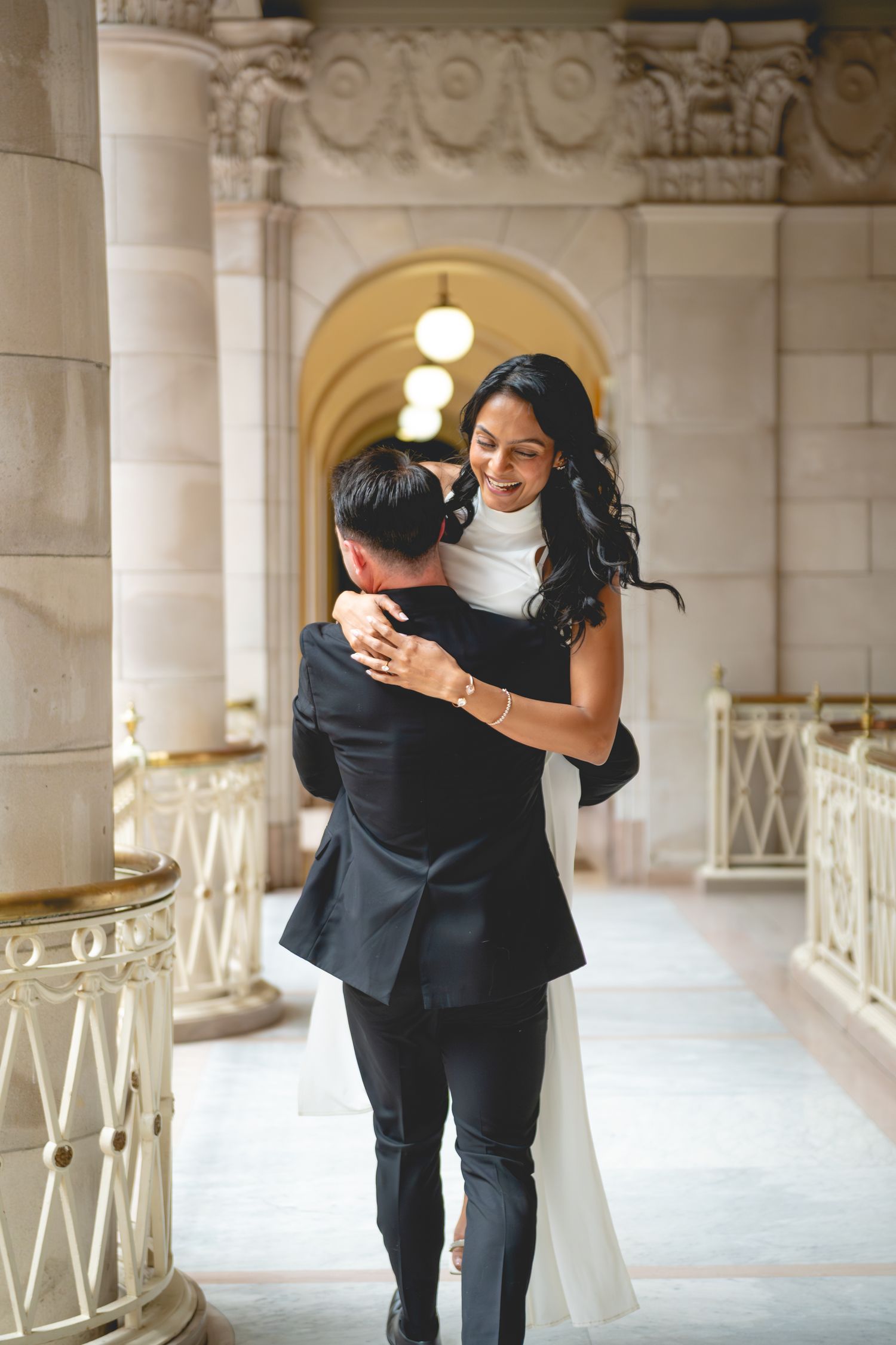 A playful couple embraces in a grand hallway with ornate architectural details and columns at Hartford City Hall.