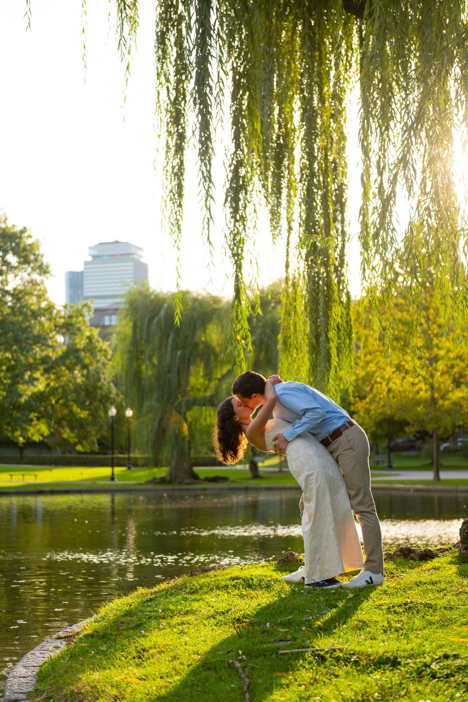 Couple embracing by a pond with weeping willow trees during golden hour at Boston Public Gardens