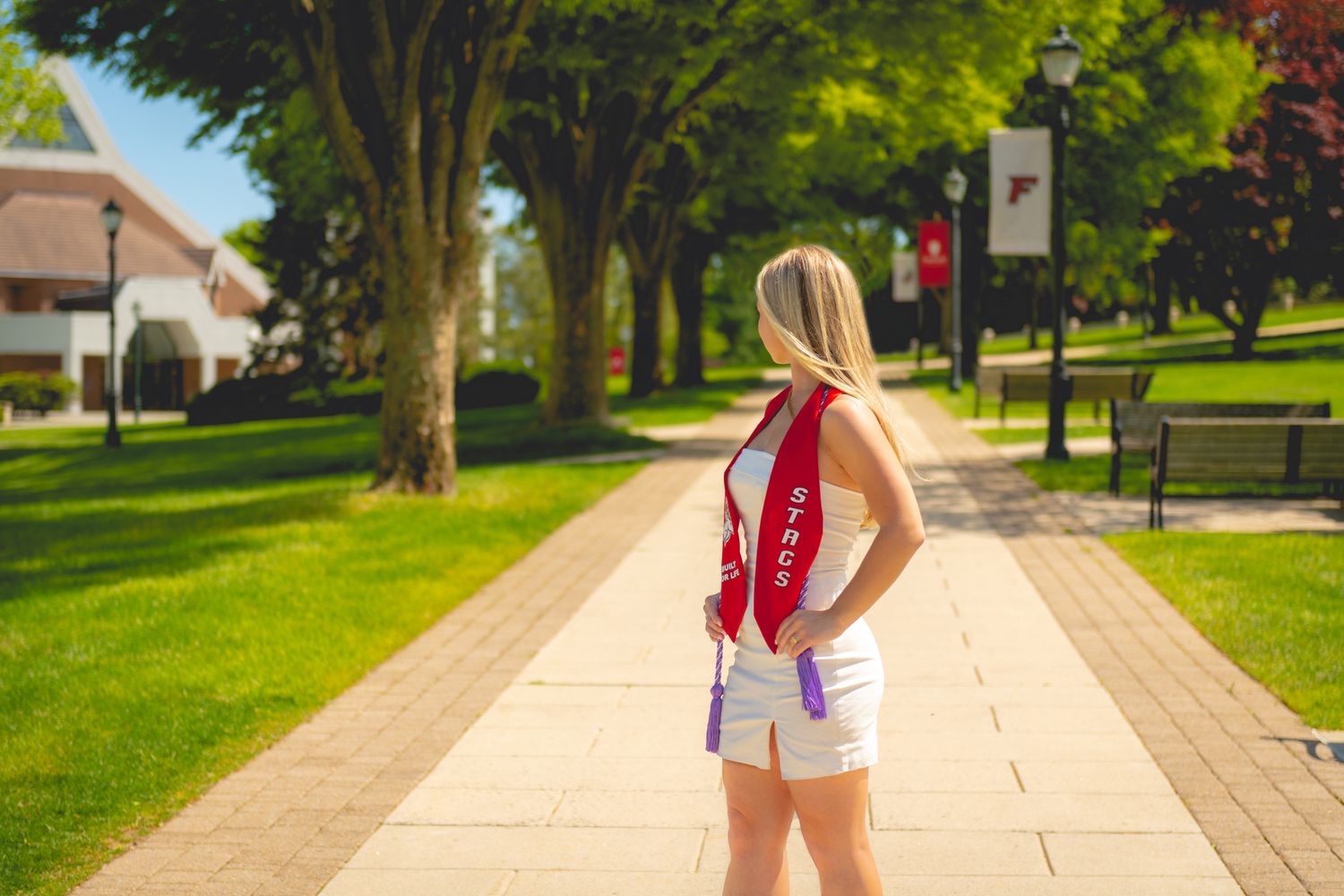 Fairfield University graduate on sunny pathway through green campus grounds.