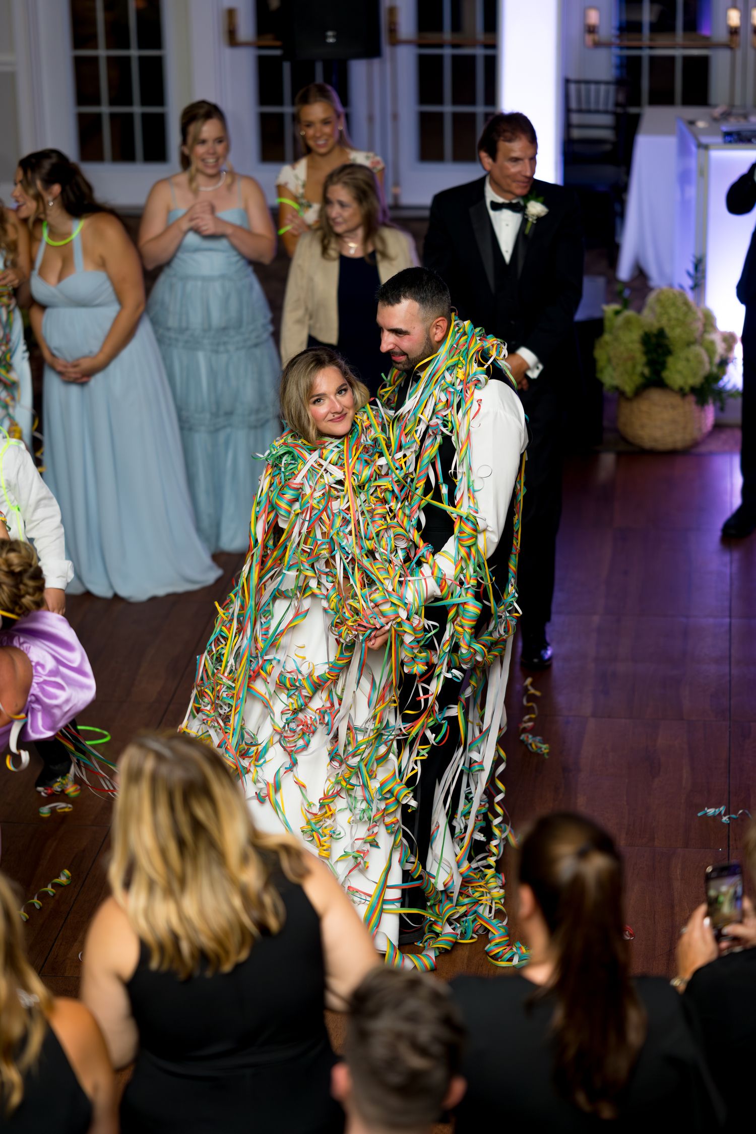 Wedding guests dancing at a reception with someone wearing a colorful metallic outfit on the dance floor.