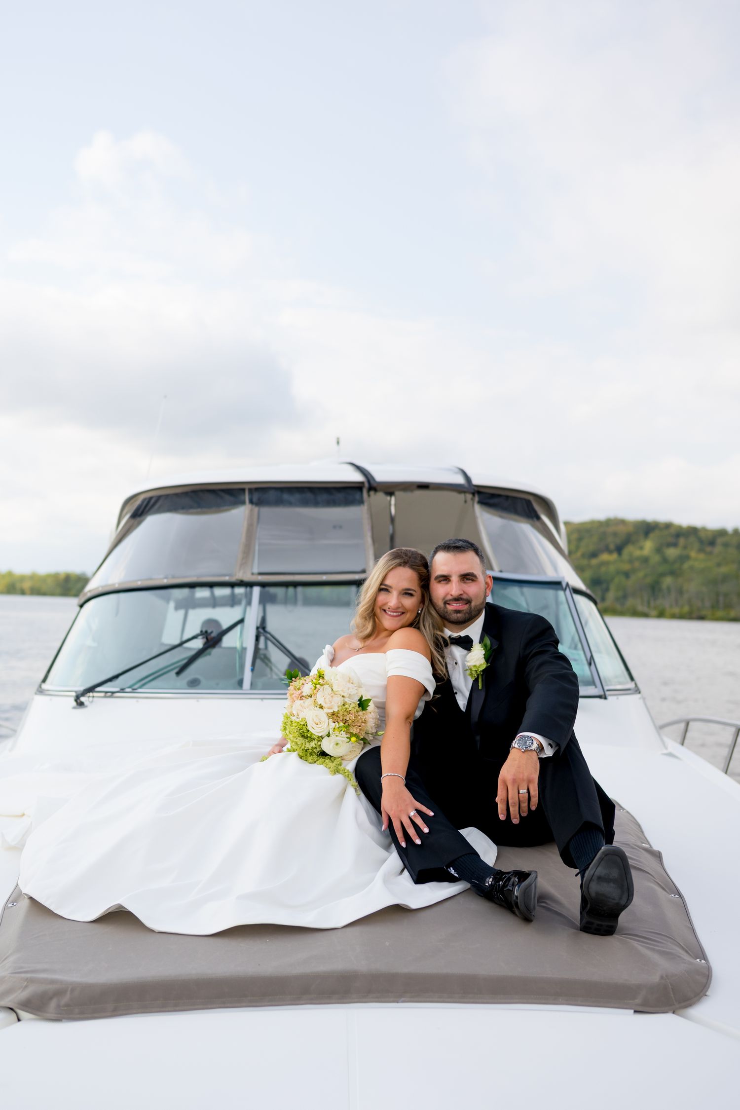 Couple relaxing on hood of vintage boat during waterfront wedding photoshoot.