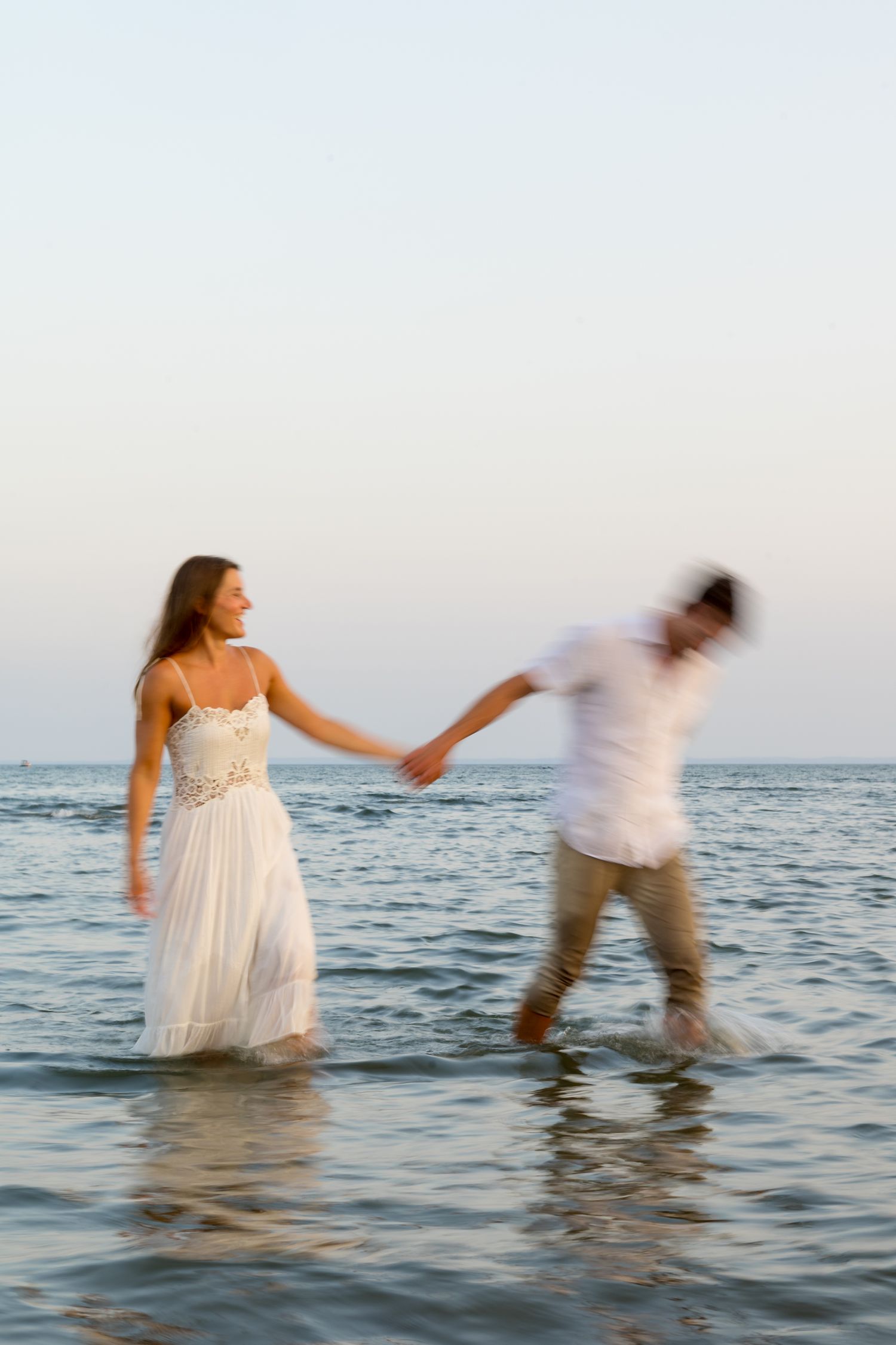 A couple splashes and plays in the ocean water during a beach photoshoot.