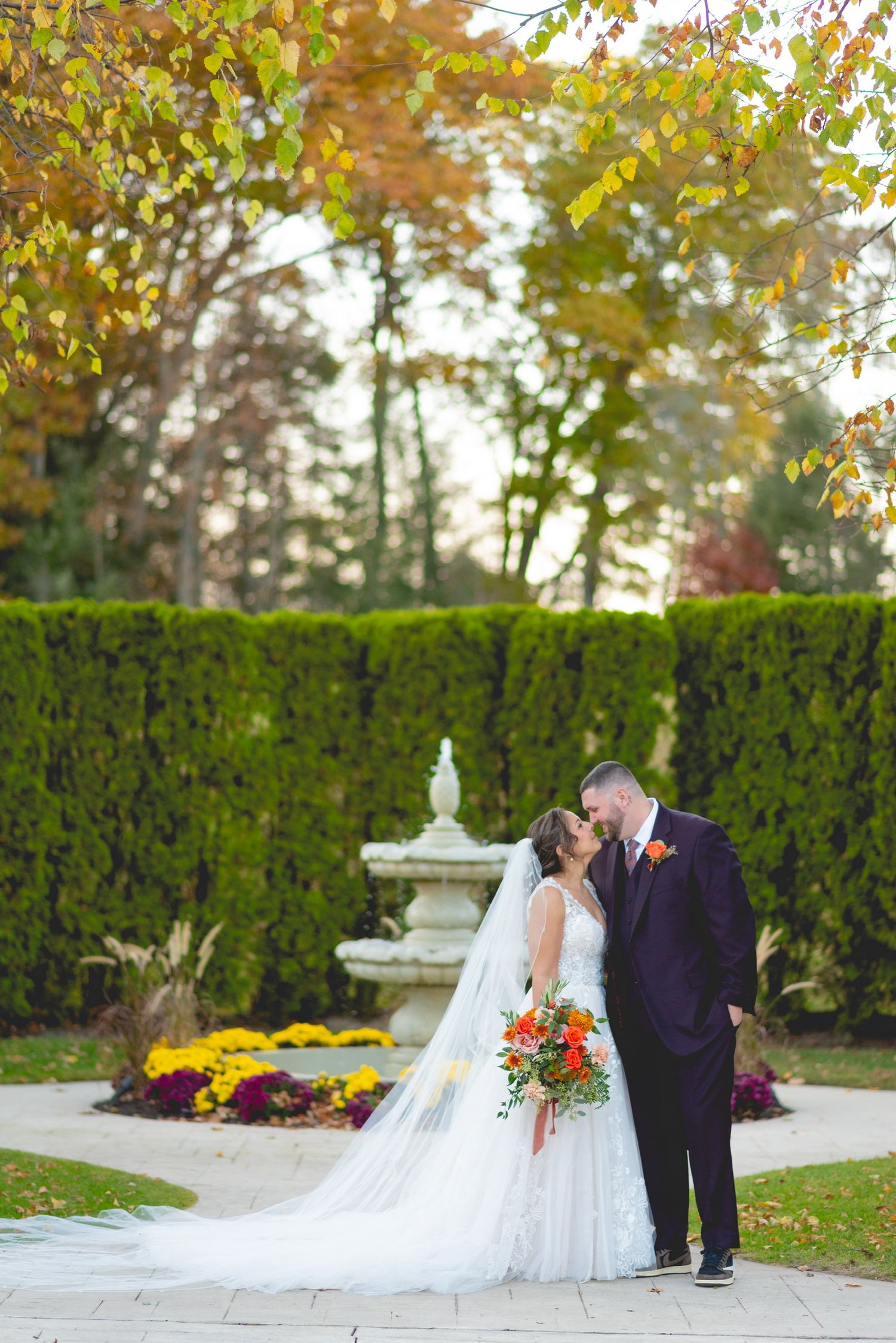 A romantic autumn wedding scene with a couple posing by a garden hedge and fountain at The Waterview in Connecticut.