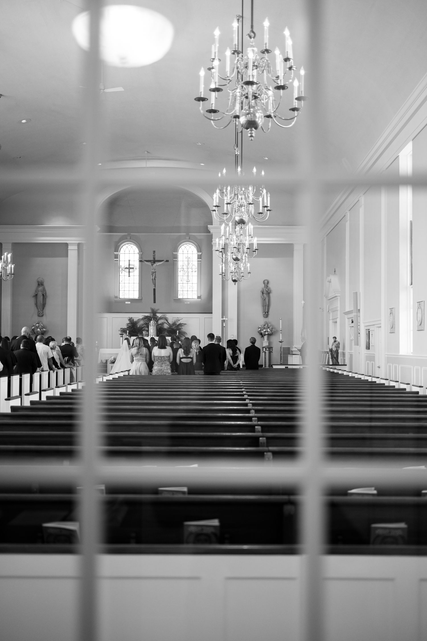 Interior of a traditional white church with wooden pews and crystal chandeliers.