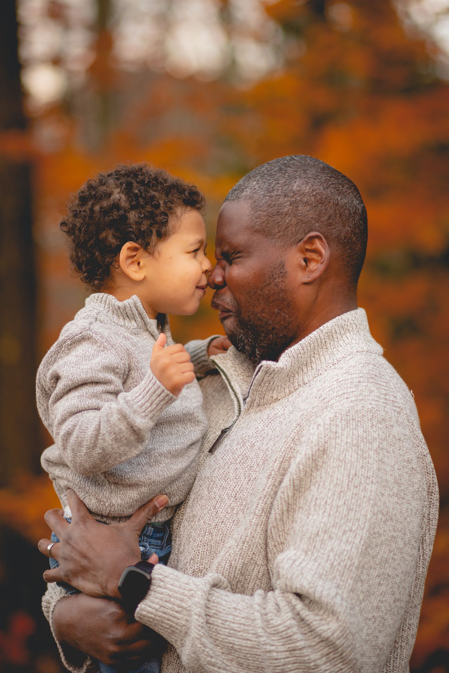 Intimate family moment captured against vibrant autumn foliage background.