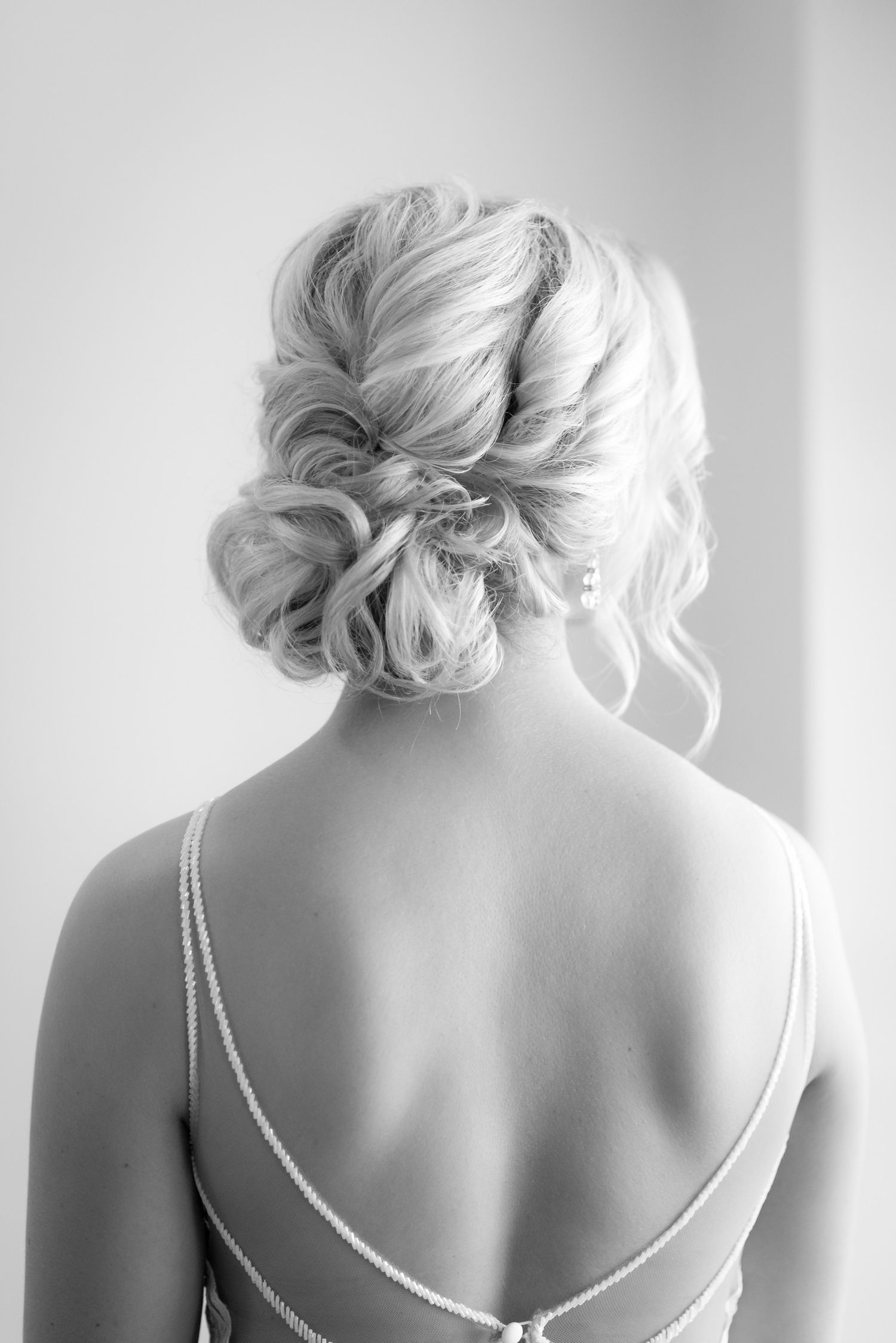 Elegant updo hairstyle with loose curls shown from behind with delicate spaghetti strap dress.