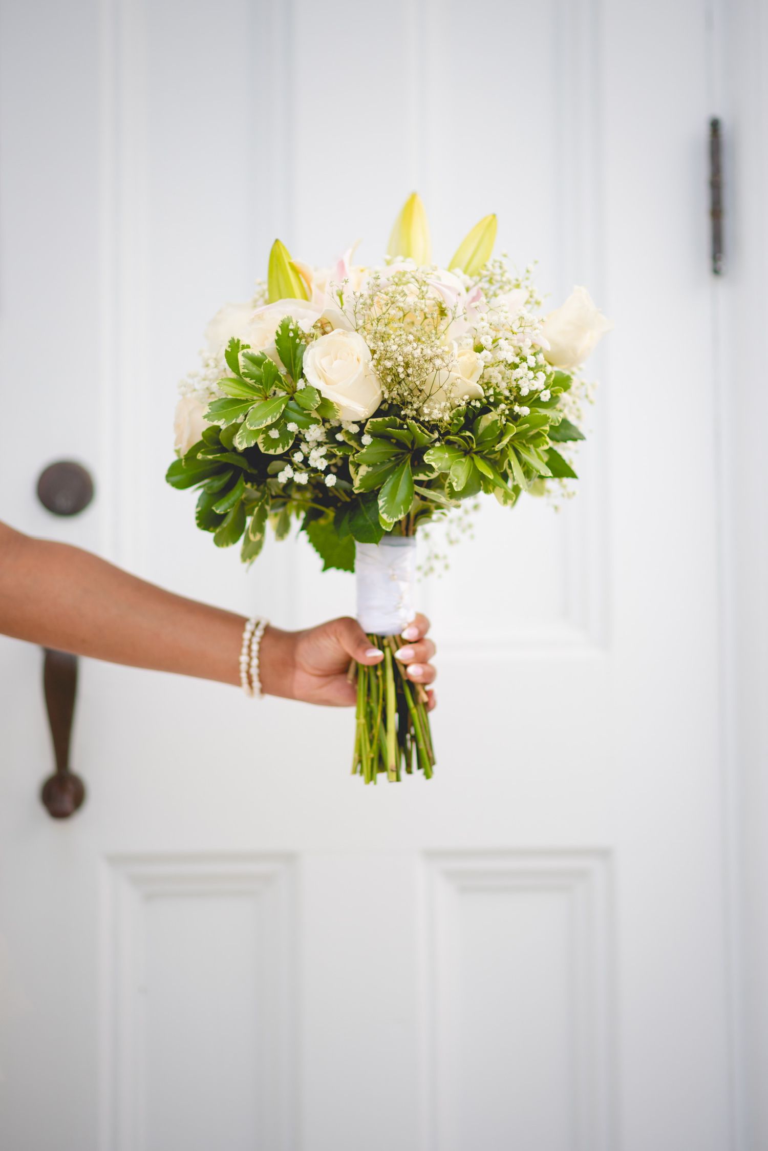 Elegant white and green wedding bouquet with roses and baby's breath against a white background.