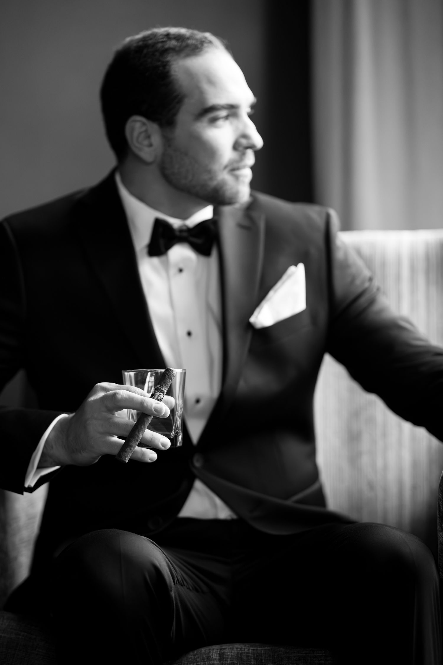 Man in tuxedo sits thoughtfully in dramatic side lighting.