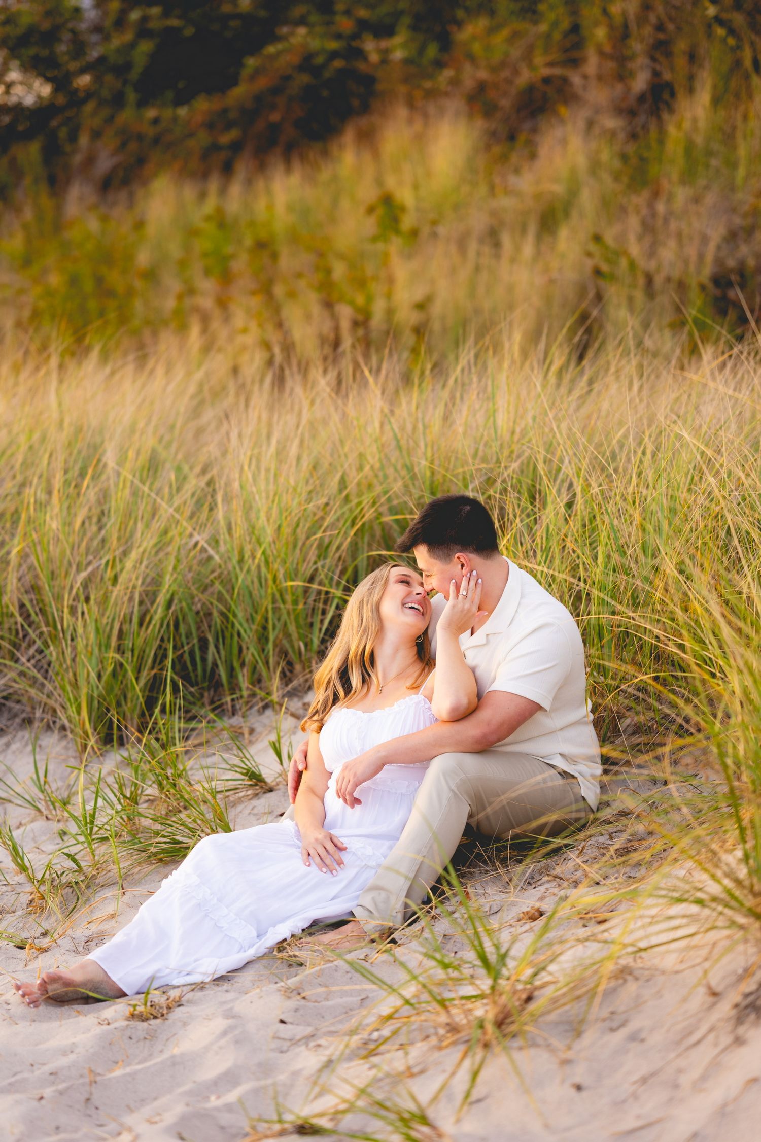 Romantic couple embracing on a sandy beach with tall grass at Harkness Memorial State Park in Waterford, Connecticut.