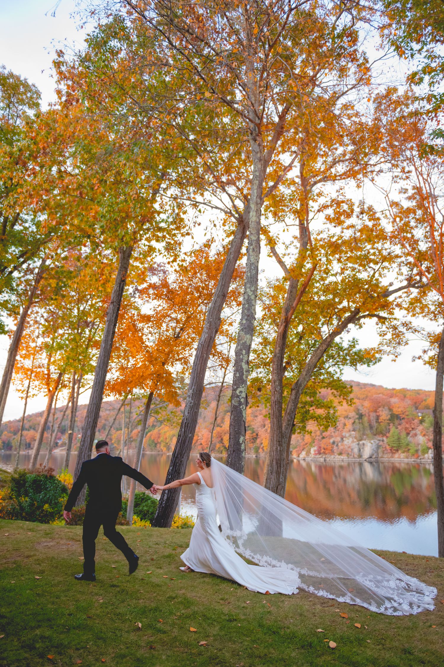 A dramatic wedding veil flowing in the breeze against autumn trees and a lakeside backdrop at The Waterview in Connecticut.