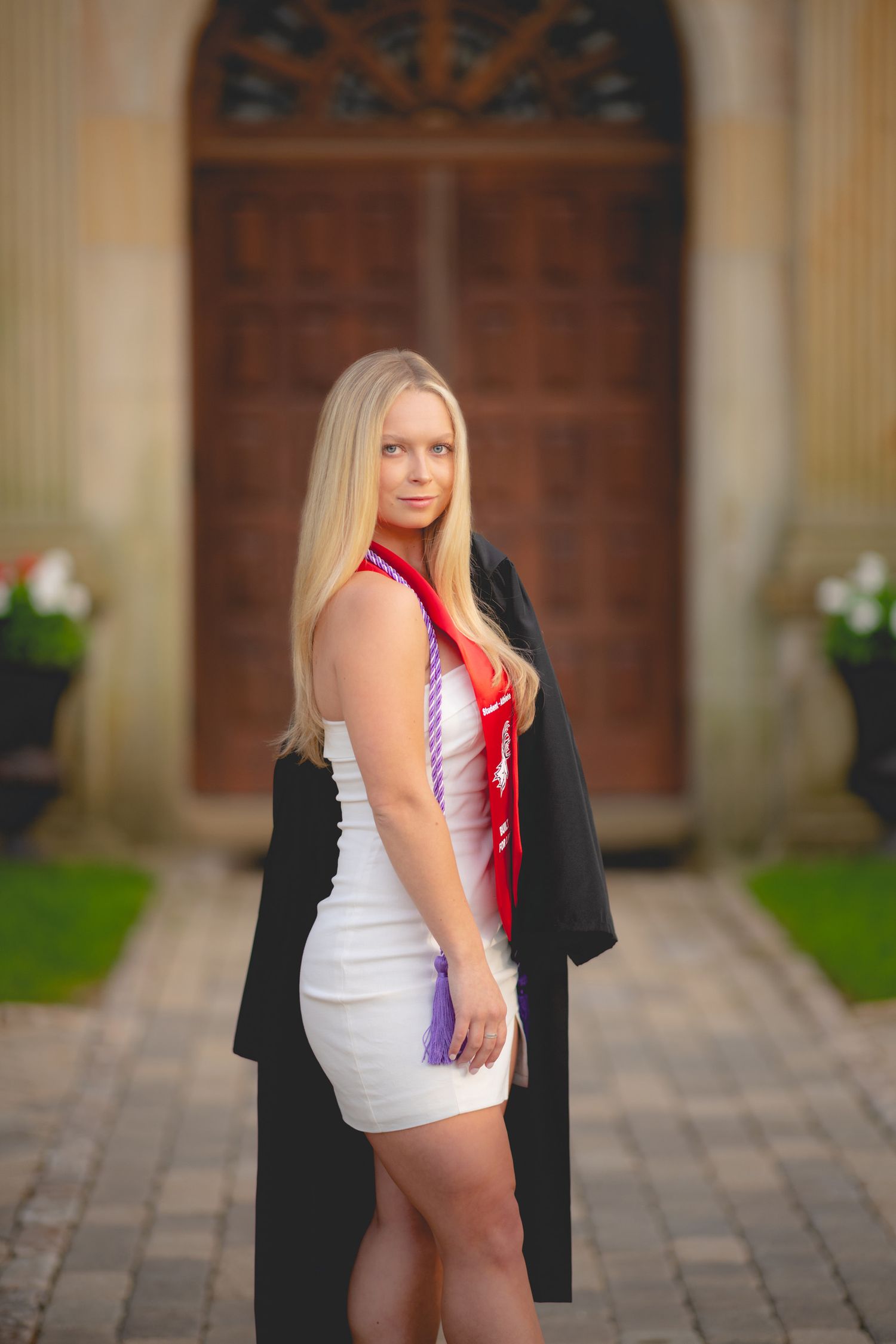 Fairfield University graduate in cap and gown poses against brick building entrance for graduation photo.