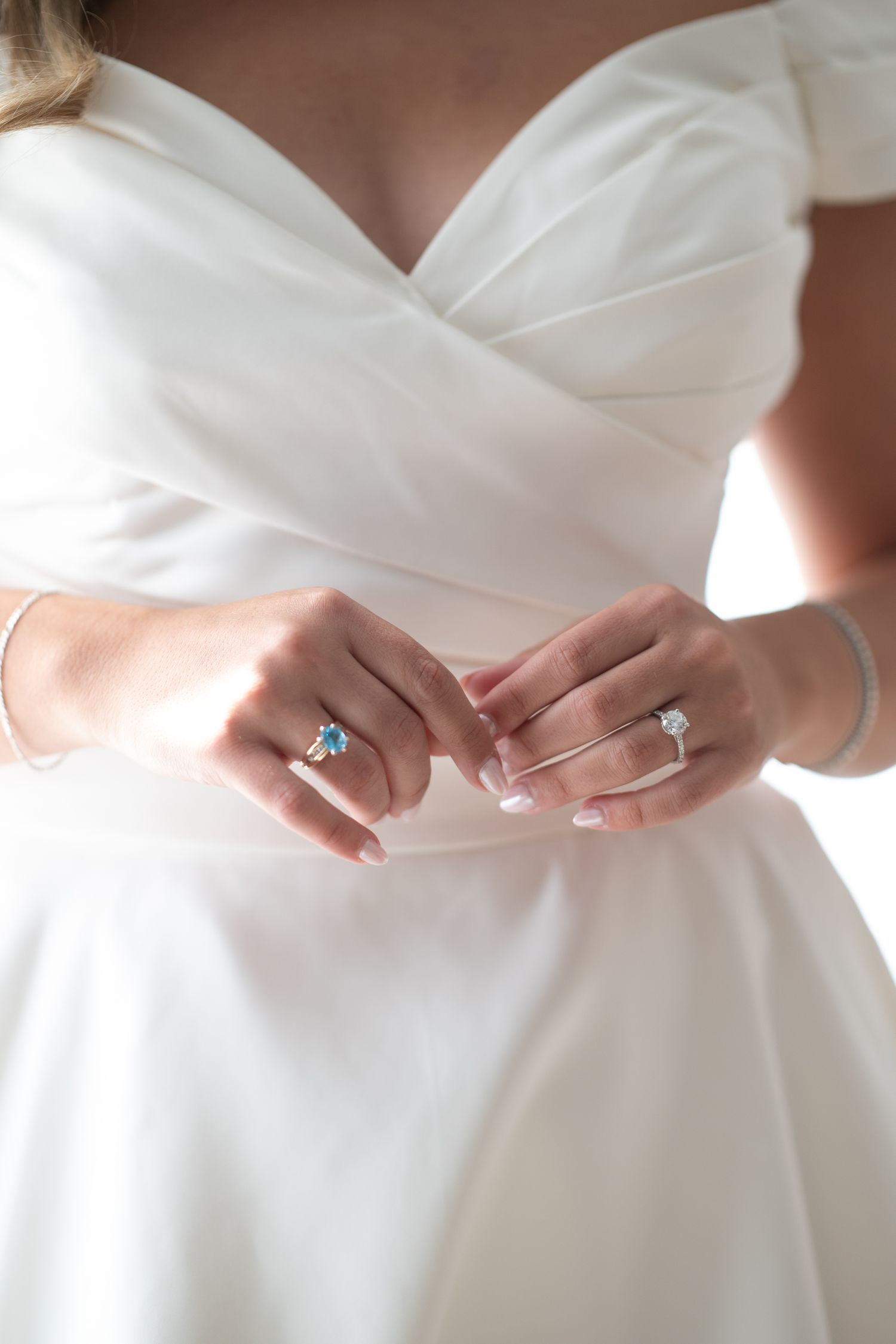 Close-up detail of hands adjusting a white wedding dress, showing delicate fabric and an engagement ring.