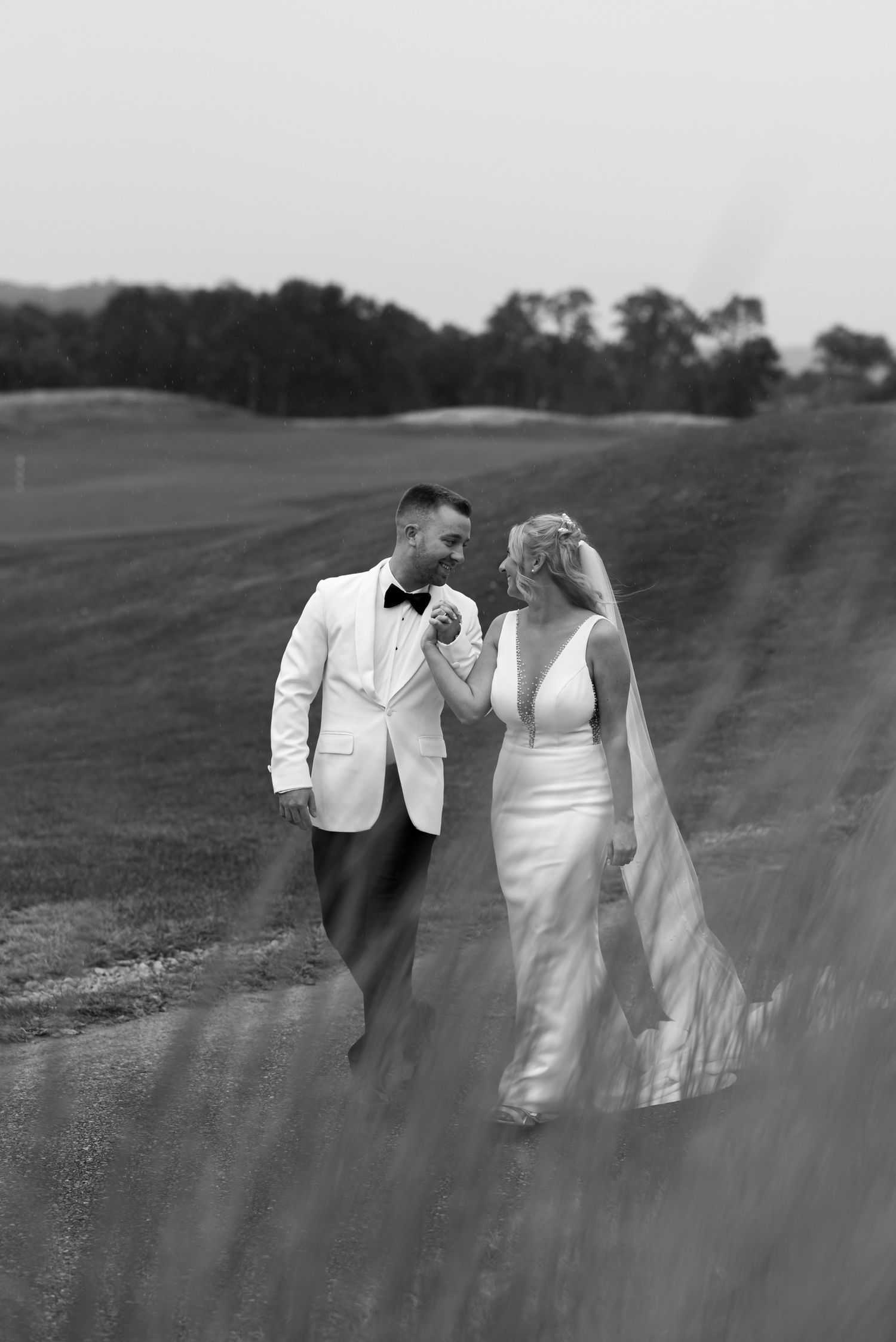 A romantic black and white wedding portrait captured through flowing grass.