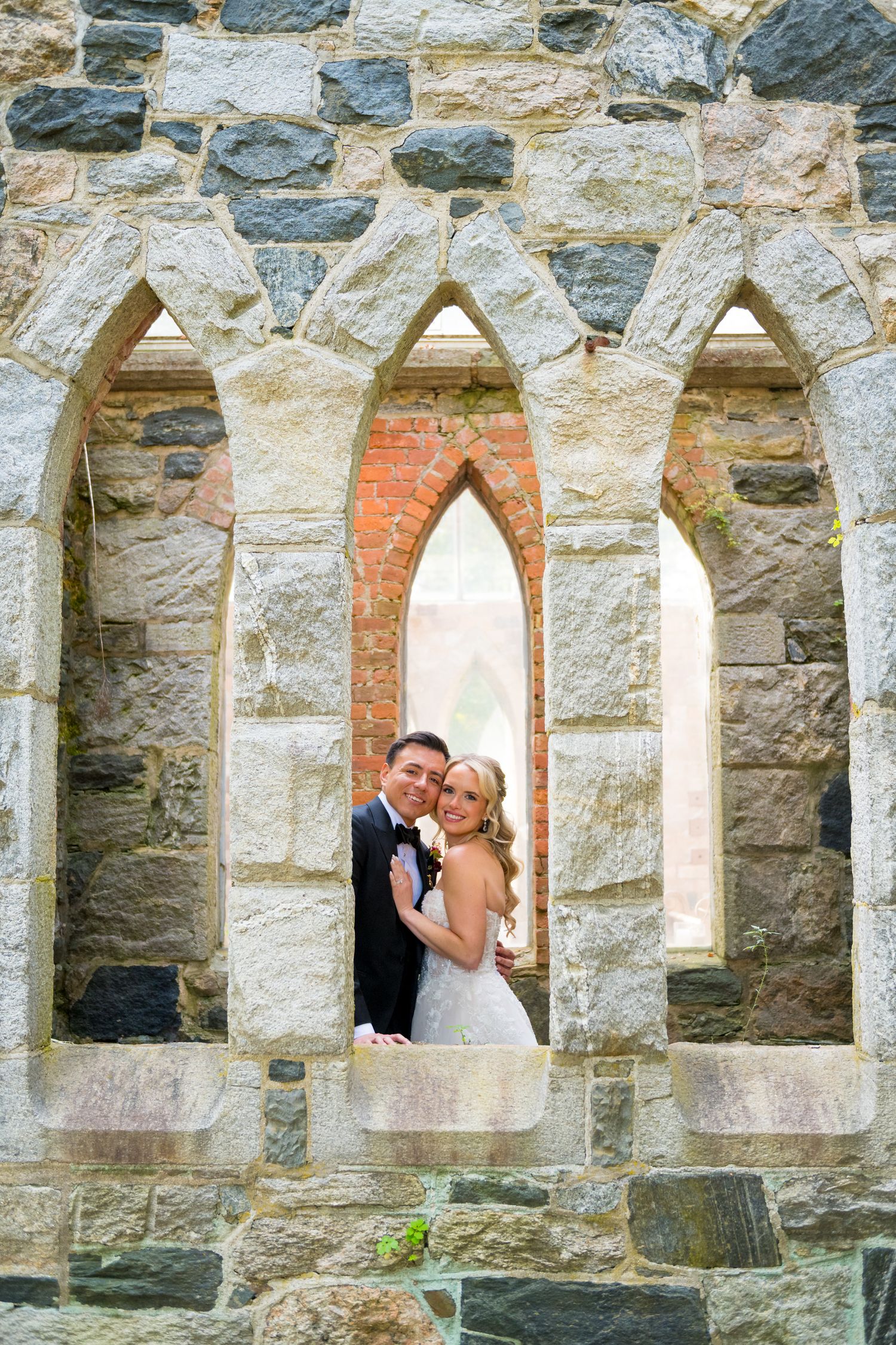 Stone archways with gothic windows frame a romantic moment at a historic venue.