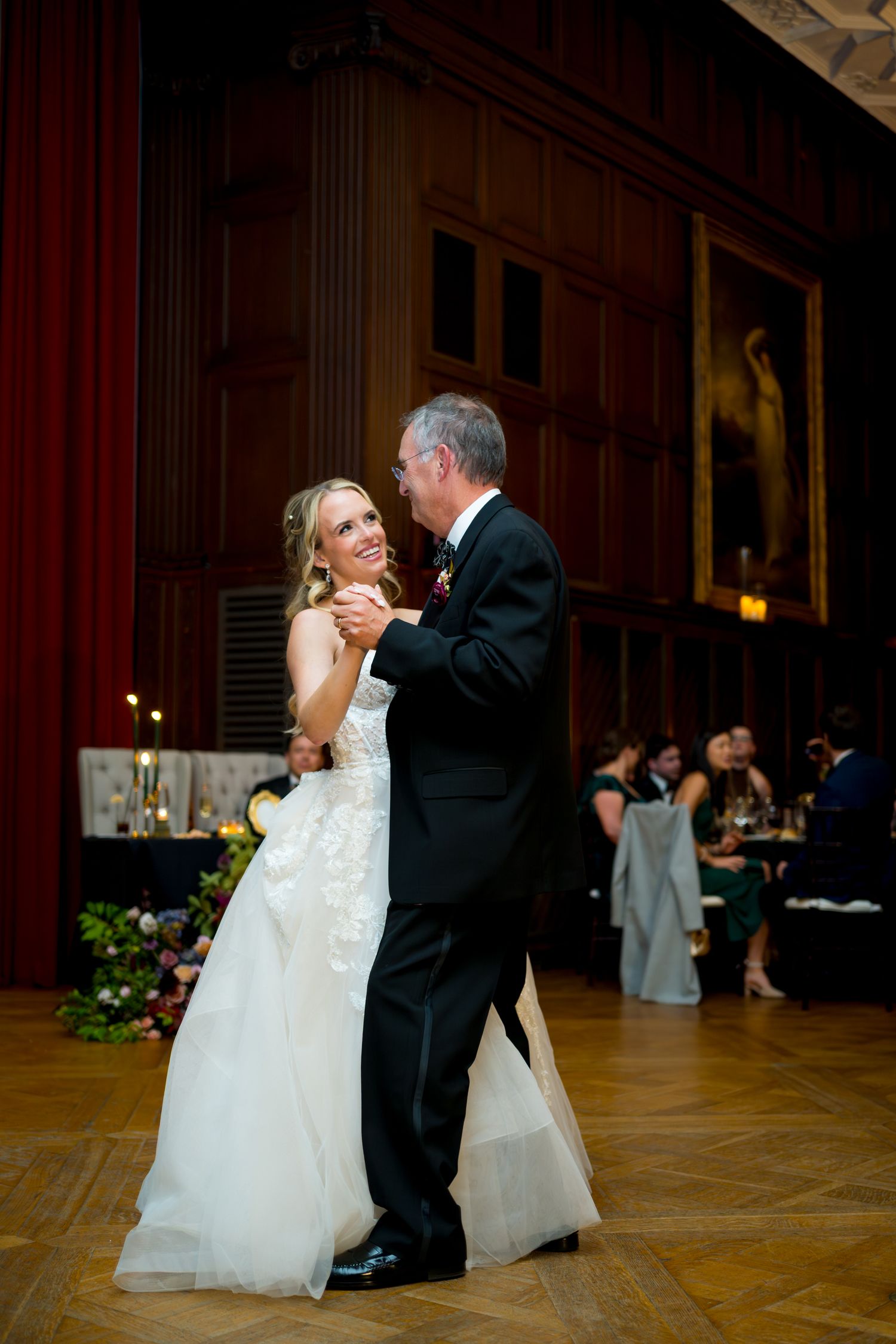 Newlyweds share their first dance on a grand ballroom floor surrounded by romantic lighting and decor.