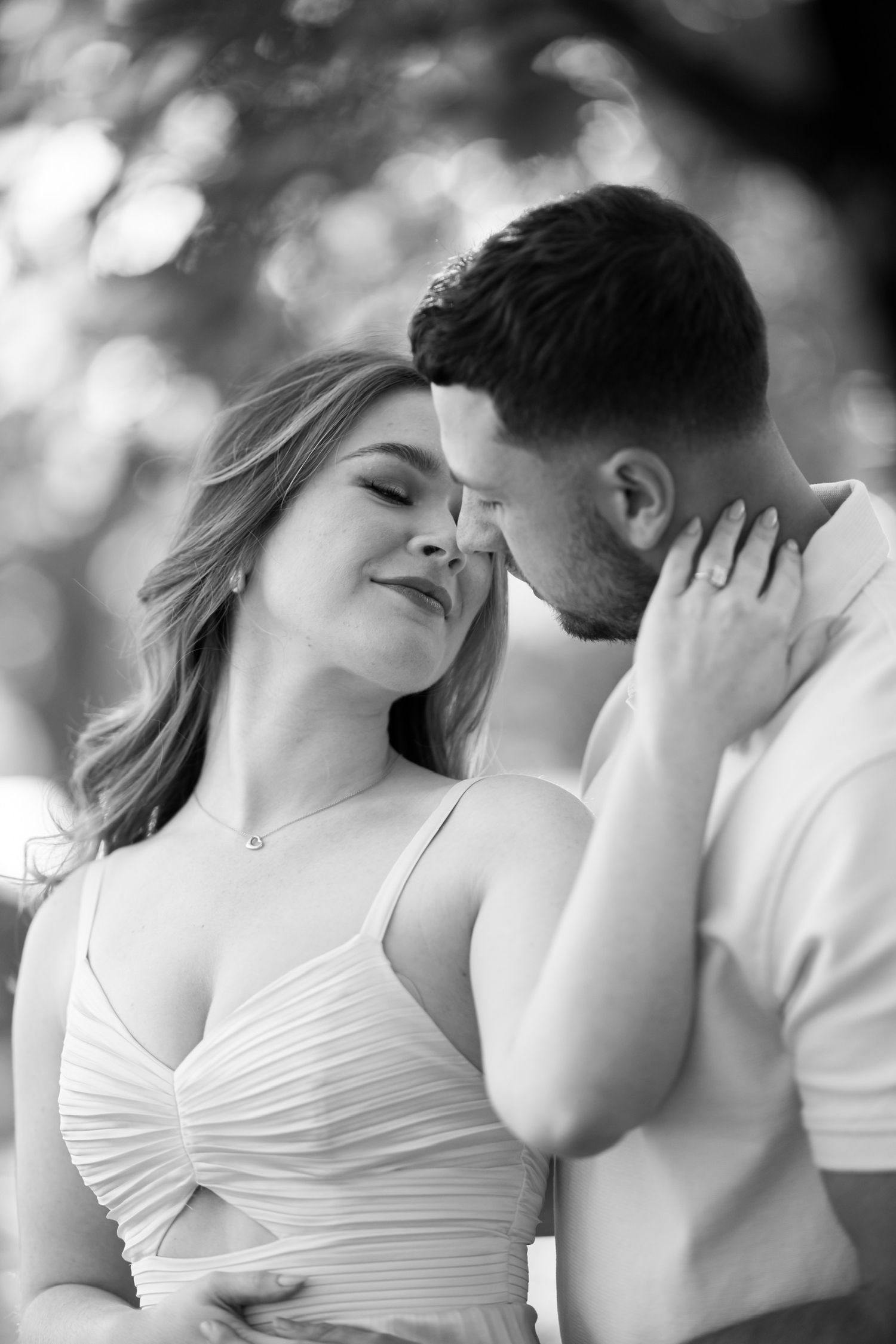 Intimate black and white portrait of a couple sharing a tender romantic moment outdoors.