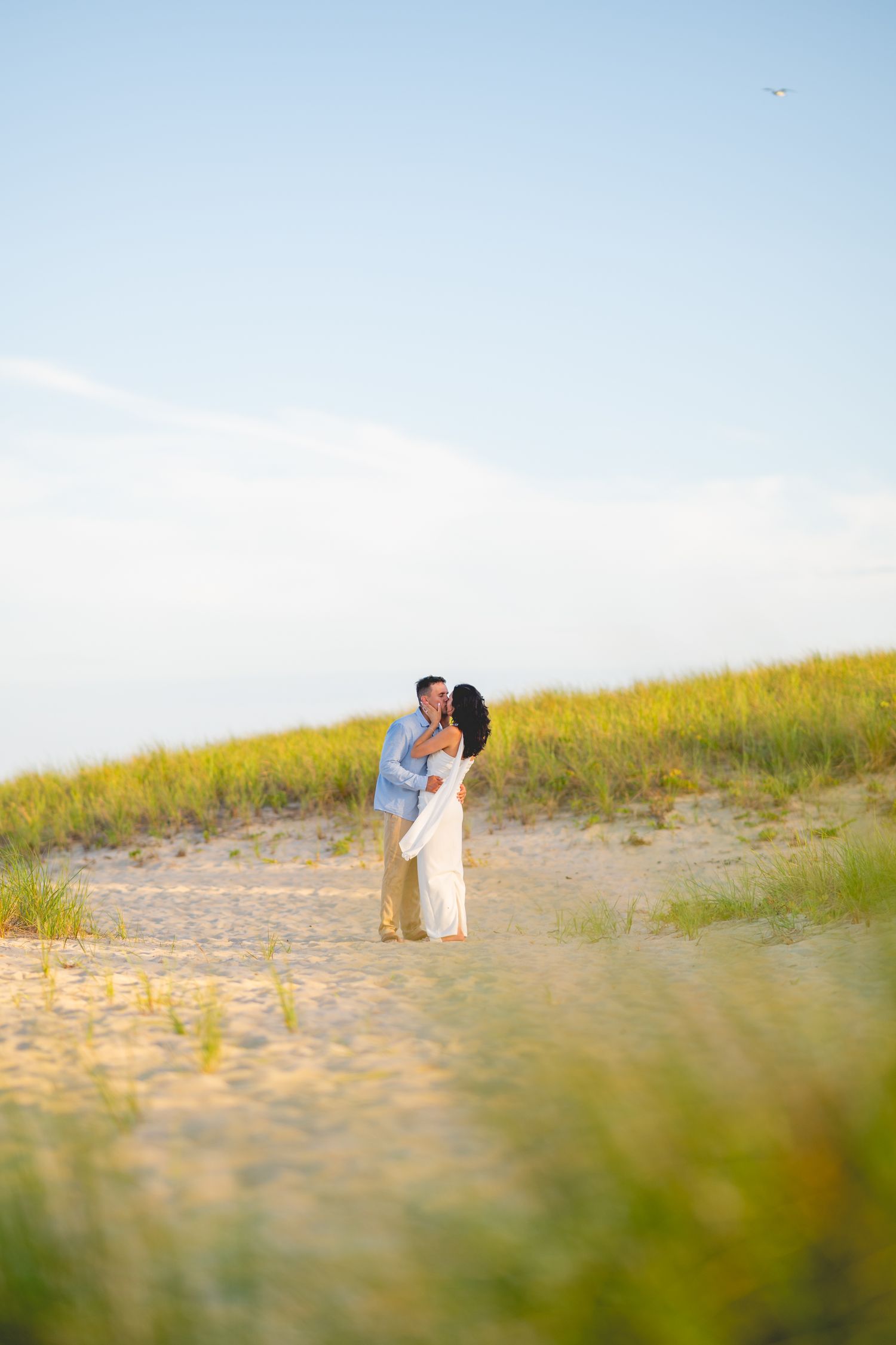A romantic beachside scene with a couple against sand dunes and golden light at Chatham Lighthouse Beach in Chatham, Massachusetts.